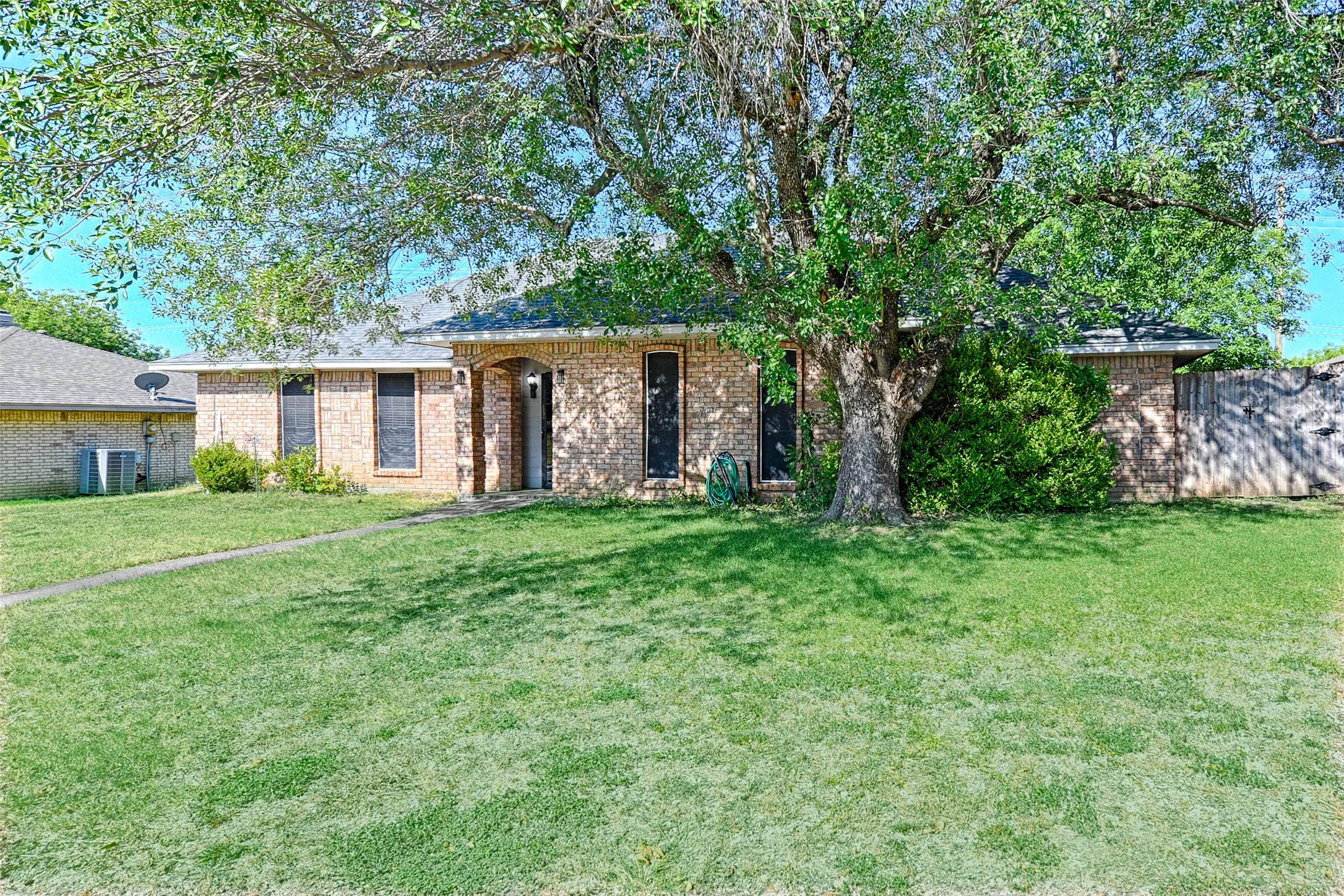 Brick exterior featuring an arched entry, mature trees, and a spacious front lawn
