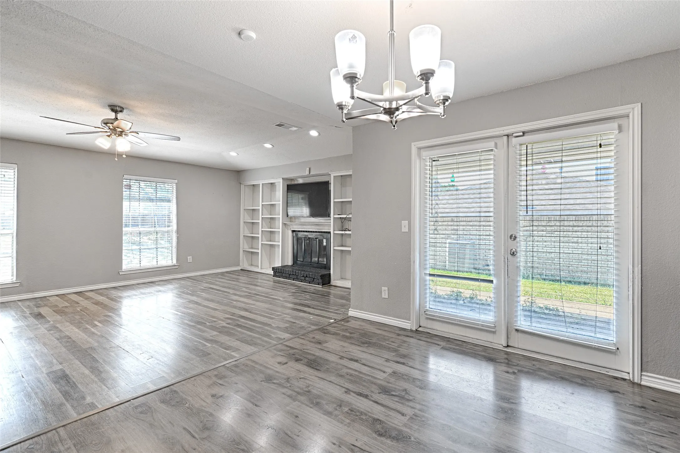 Spacious room with wood-finish flooring, a built-in fireplace with shelving, and double glass panel doors