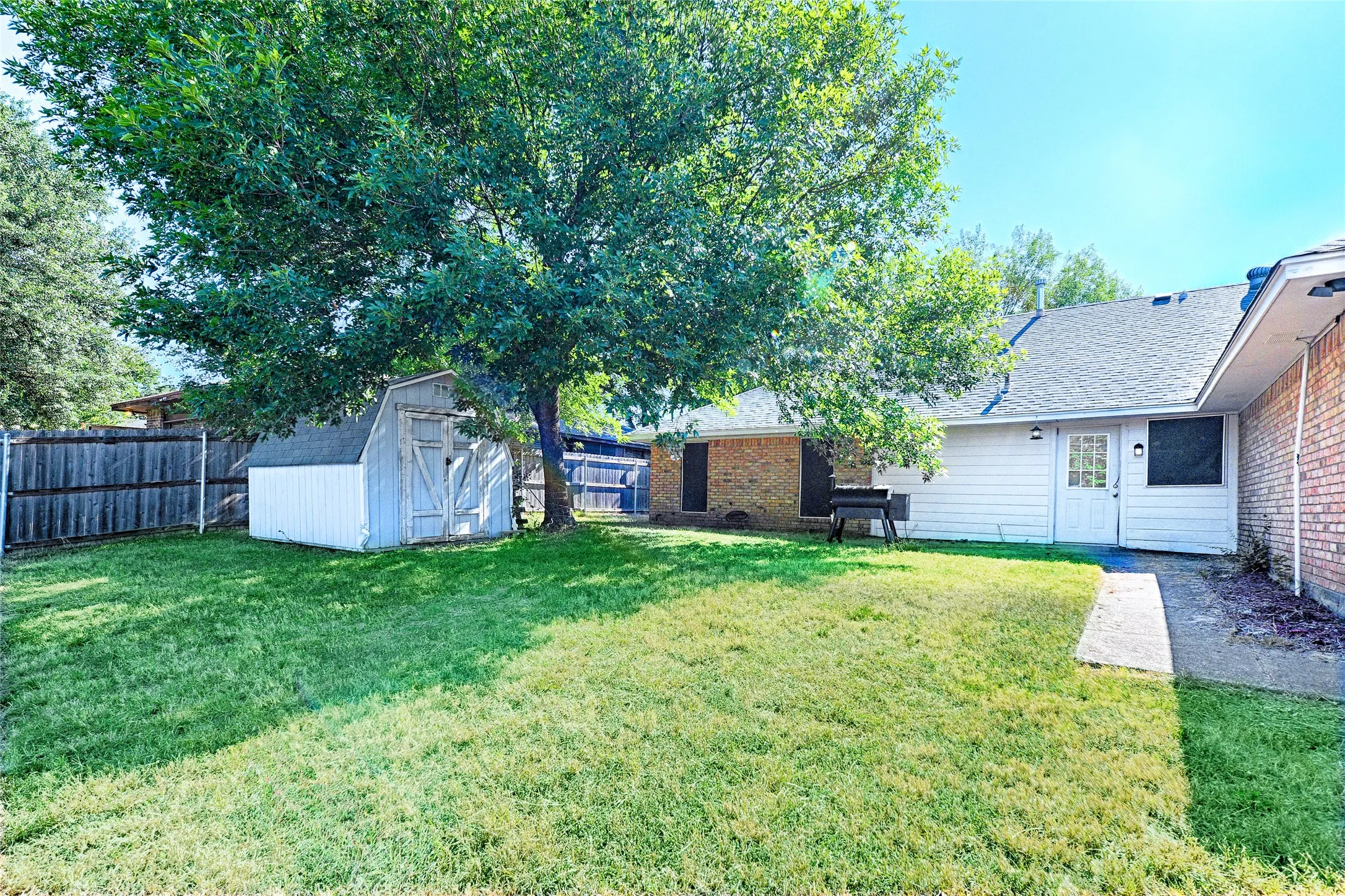 Expansive backyard with a large shade tree, wood privacy fencing, and a storage shed