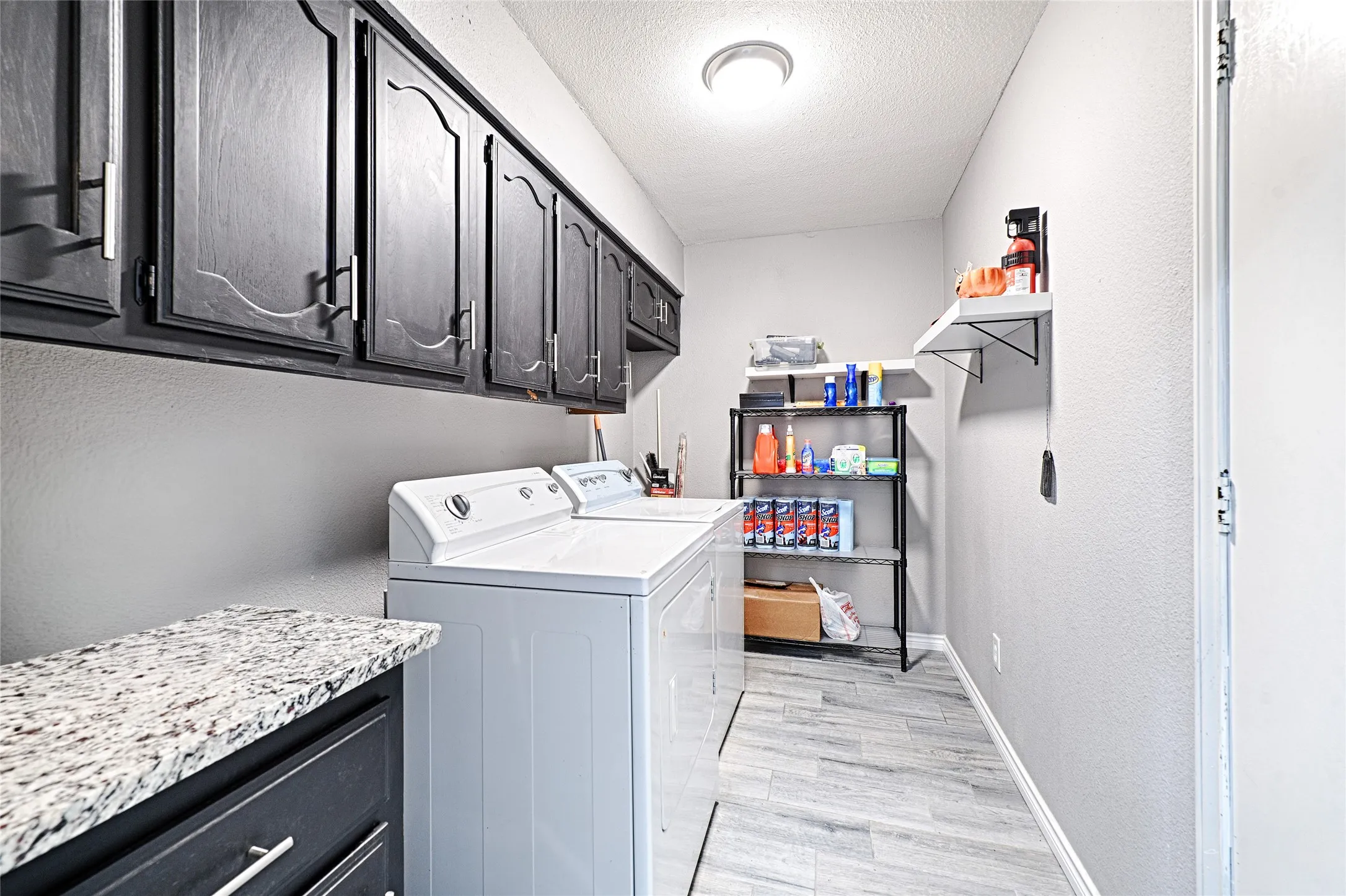 Laundry area with abundant upper cabinetry, a counter surface with a light-toned stone finish, and wood-look flooring