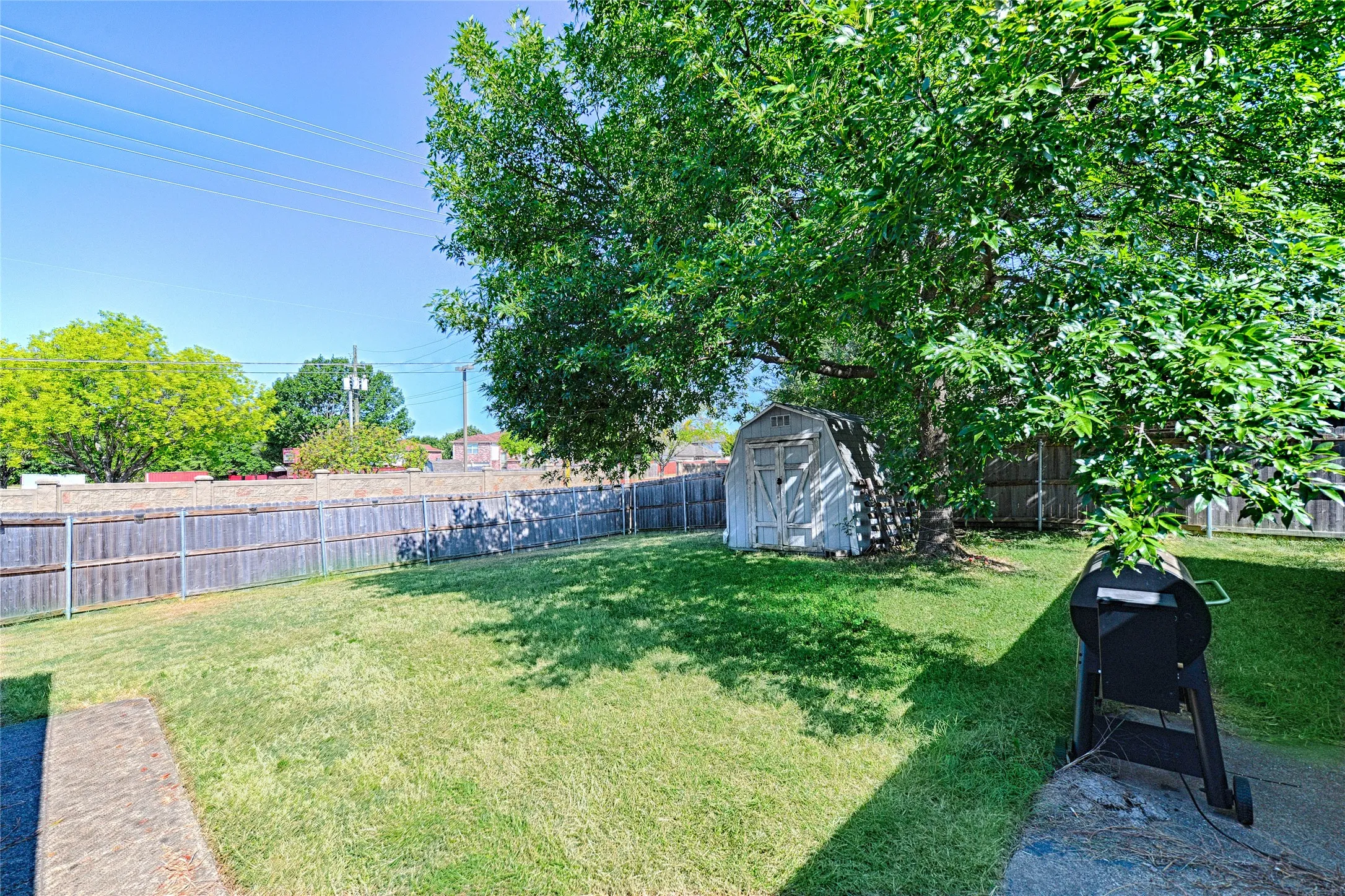 Expansive fenced backyard featuring a storage shed and mature trees