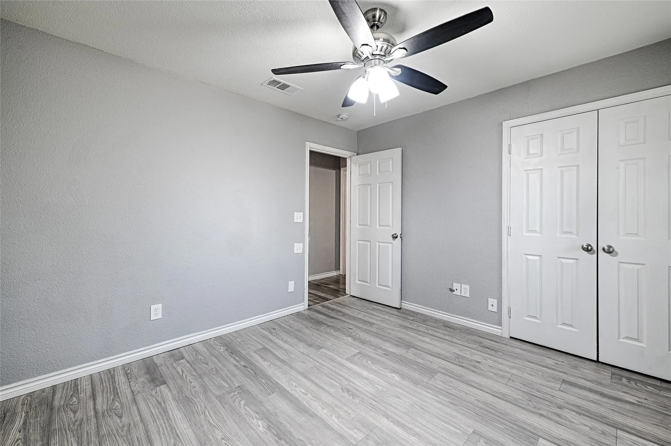 Wood-finish flooring, light gray wall tones, ceiling fan with integrated lighting, and white paneled doors