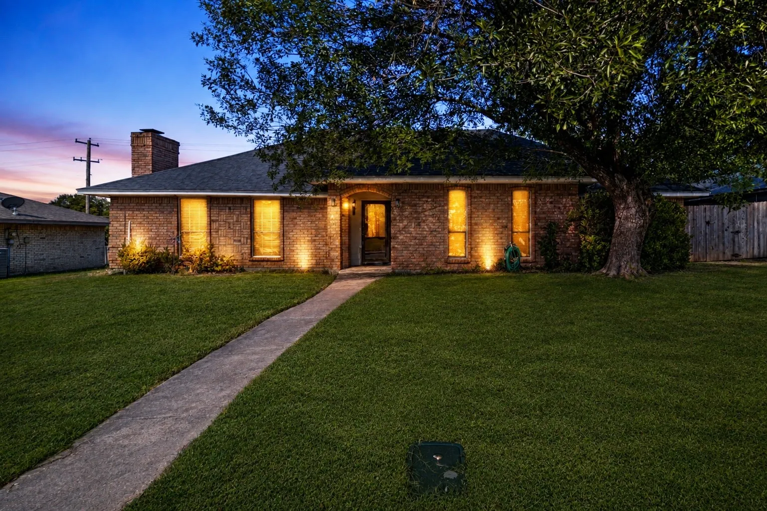 Brick exterior with a dark shingle roof, concrete walkway, and a manicured lawn