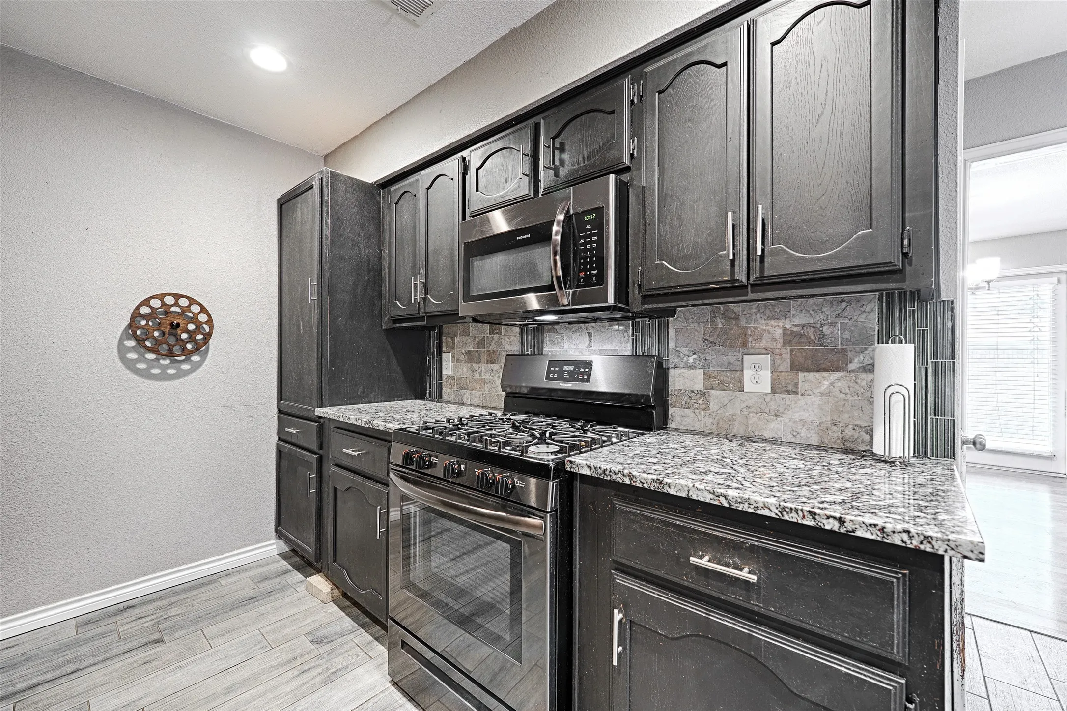 Kitchen featuring dark wood cabinetry, stainless steel appliances, speckled countertops, and a mosaic tile backsplash