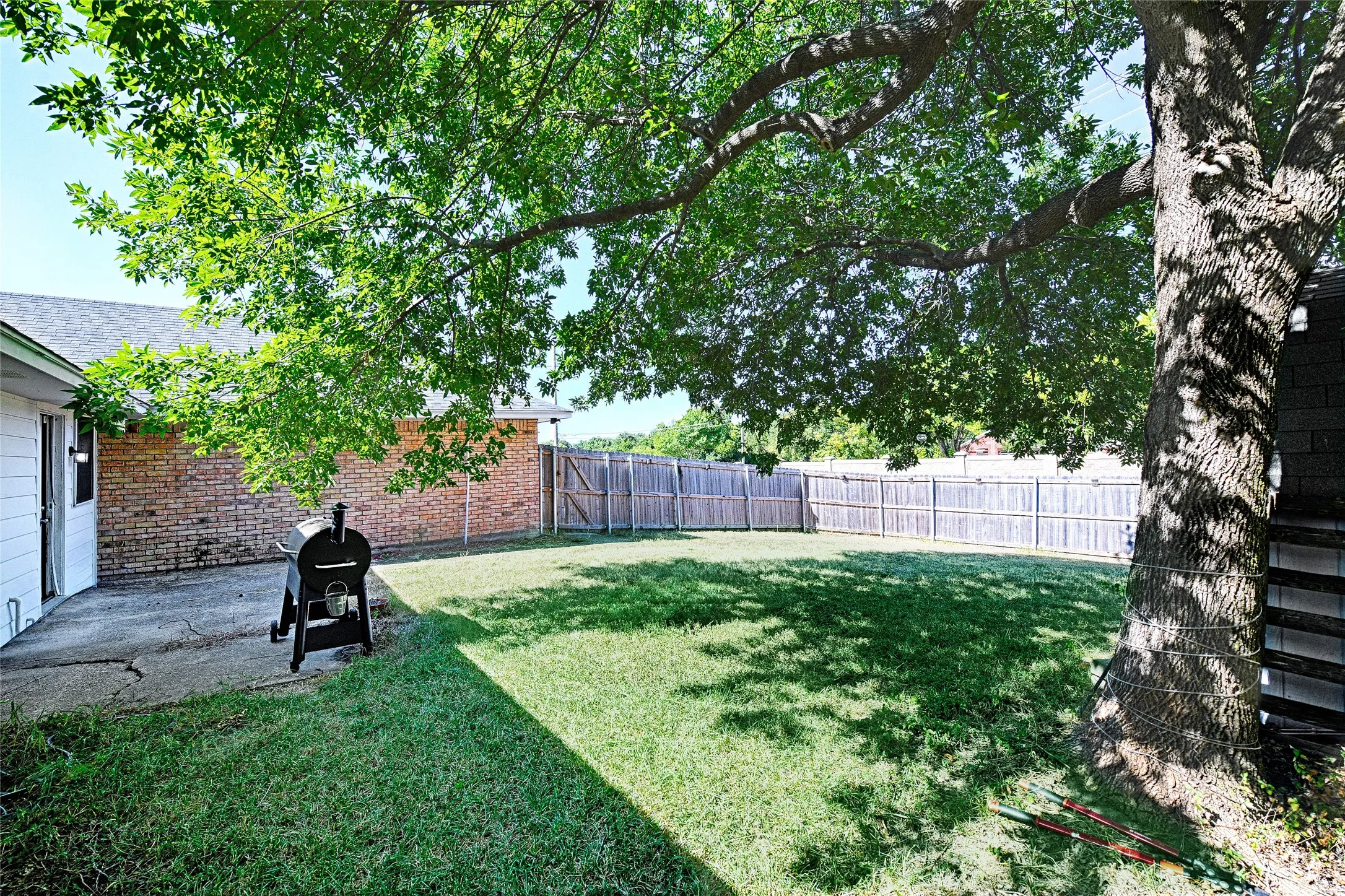 Expansive backyard with a manicured lawn, established shade tree, and wood privacy fencing