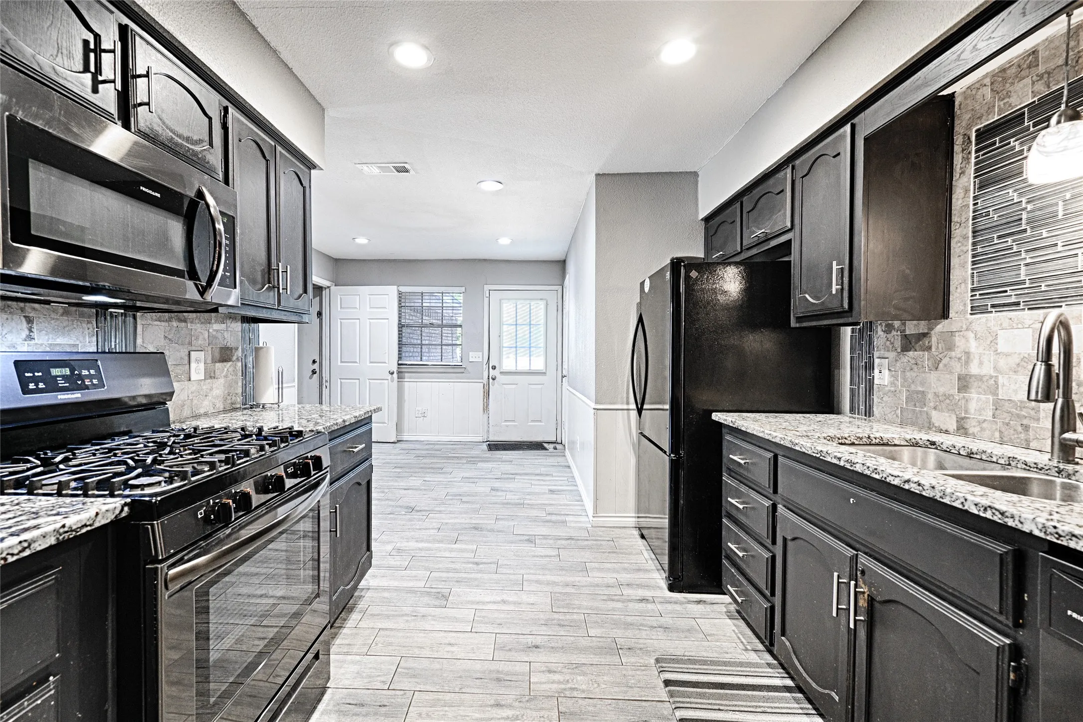 Kitchen featuring granite countertops, dark wood cabinetry, stainless steel appliances, and a tile backsplash