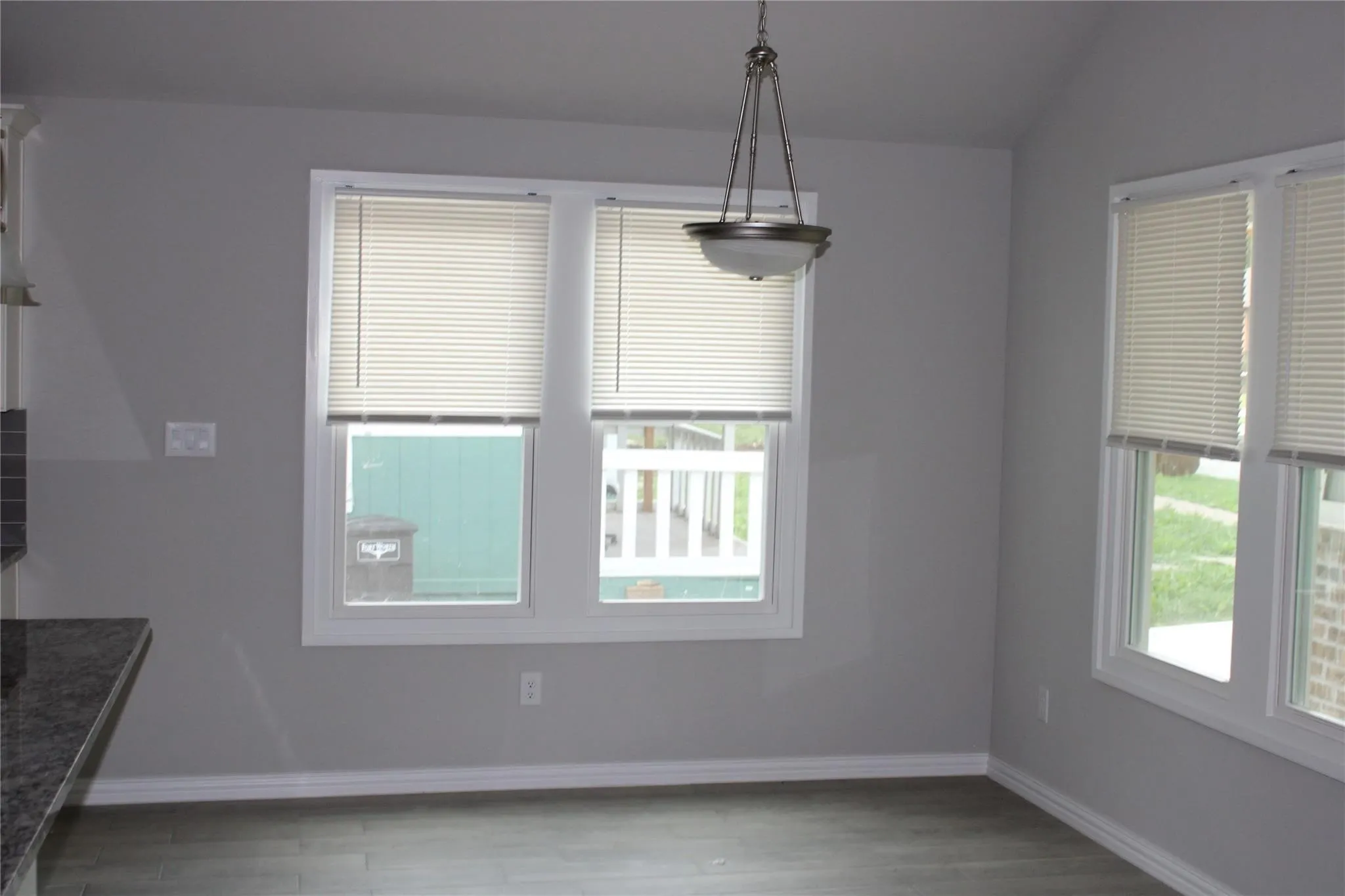 Light gray wall paint, wood-finish flooring, two large windows, white window trim, and a semi-flush mount ceiling light fixture