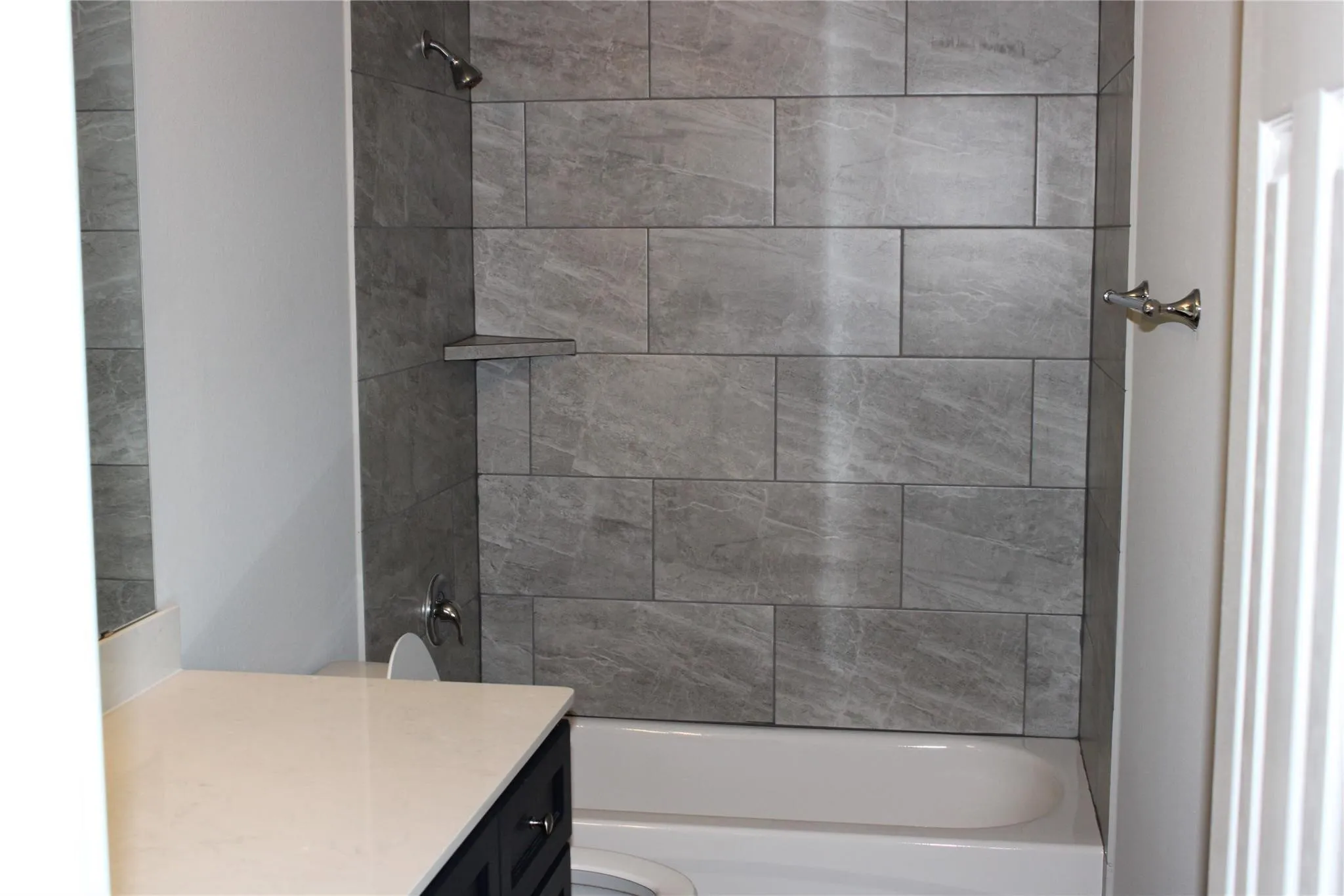 Shower/tub combination with gray tile surround, integrated corner shelf, and chrome fixtures
