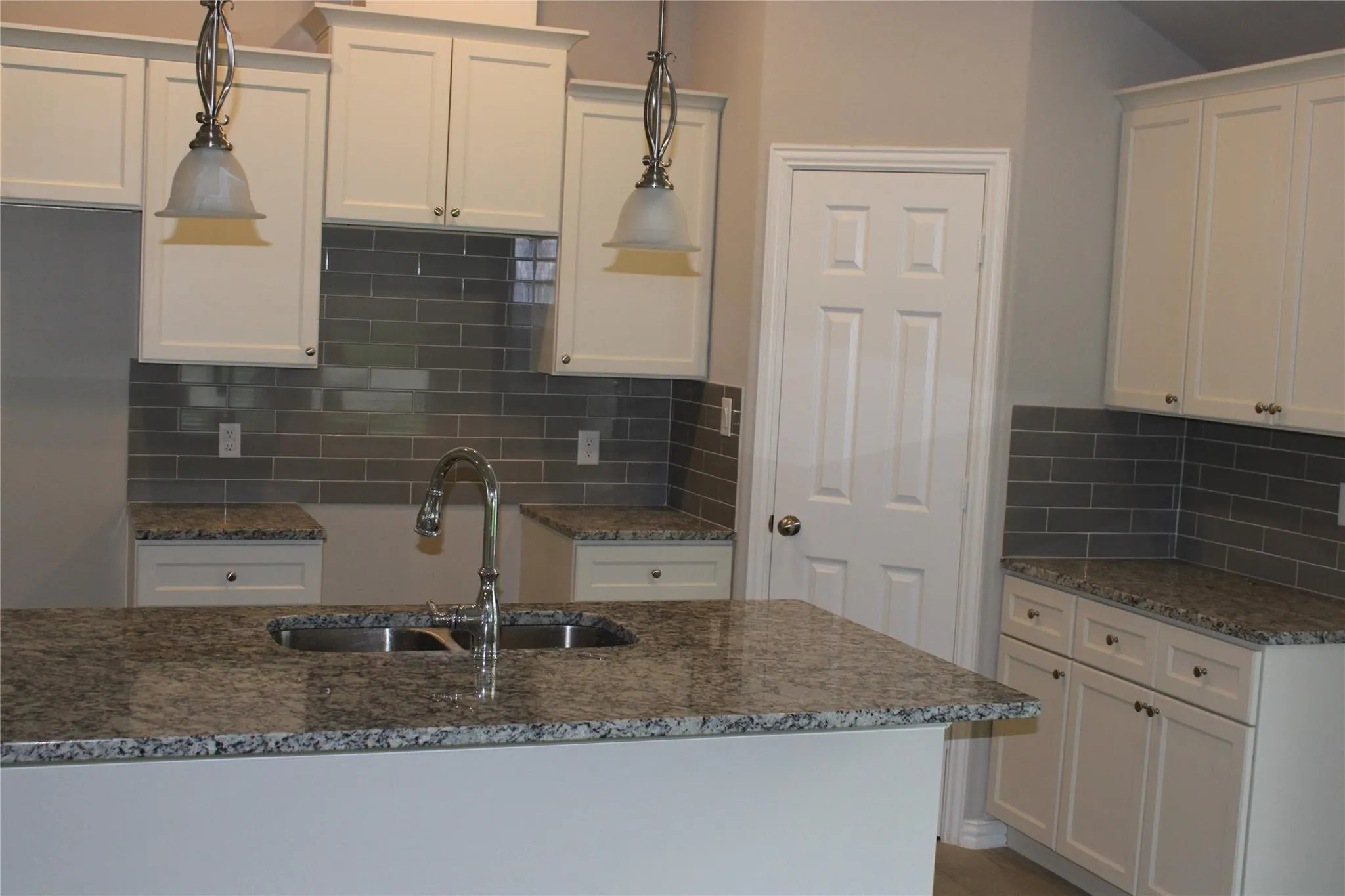 Kitchen featuring an island with a double basin sink, white cabinetry, granite-finish countertops, subway tile backsplash, and pendant lighting