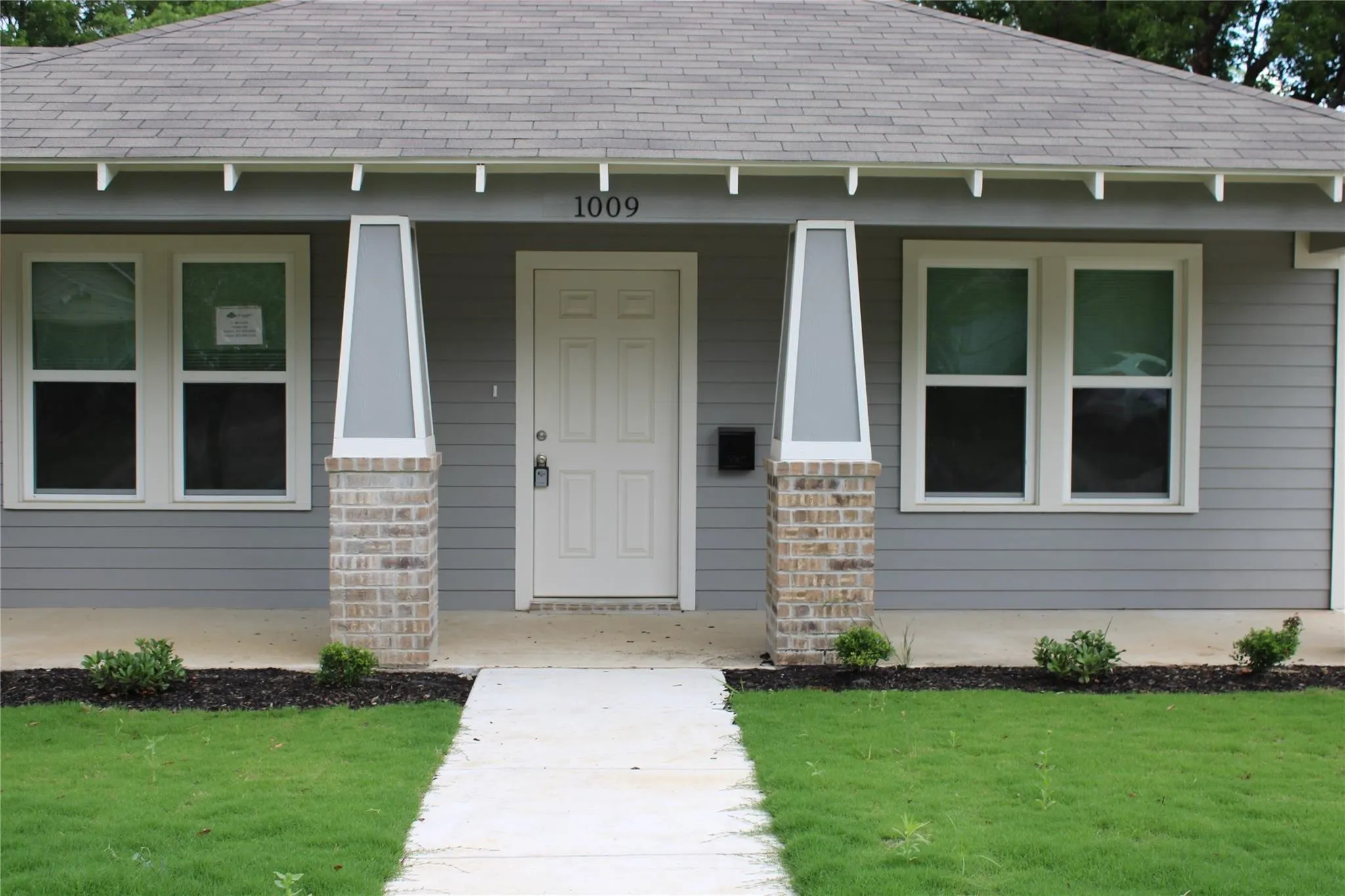 Gray siding exterior with white trim, a concrete walkway, and a covered entry