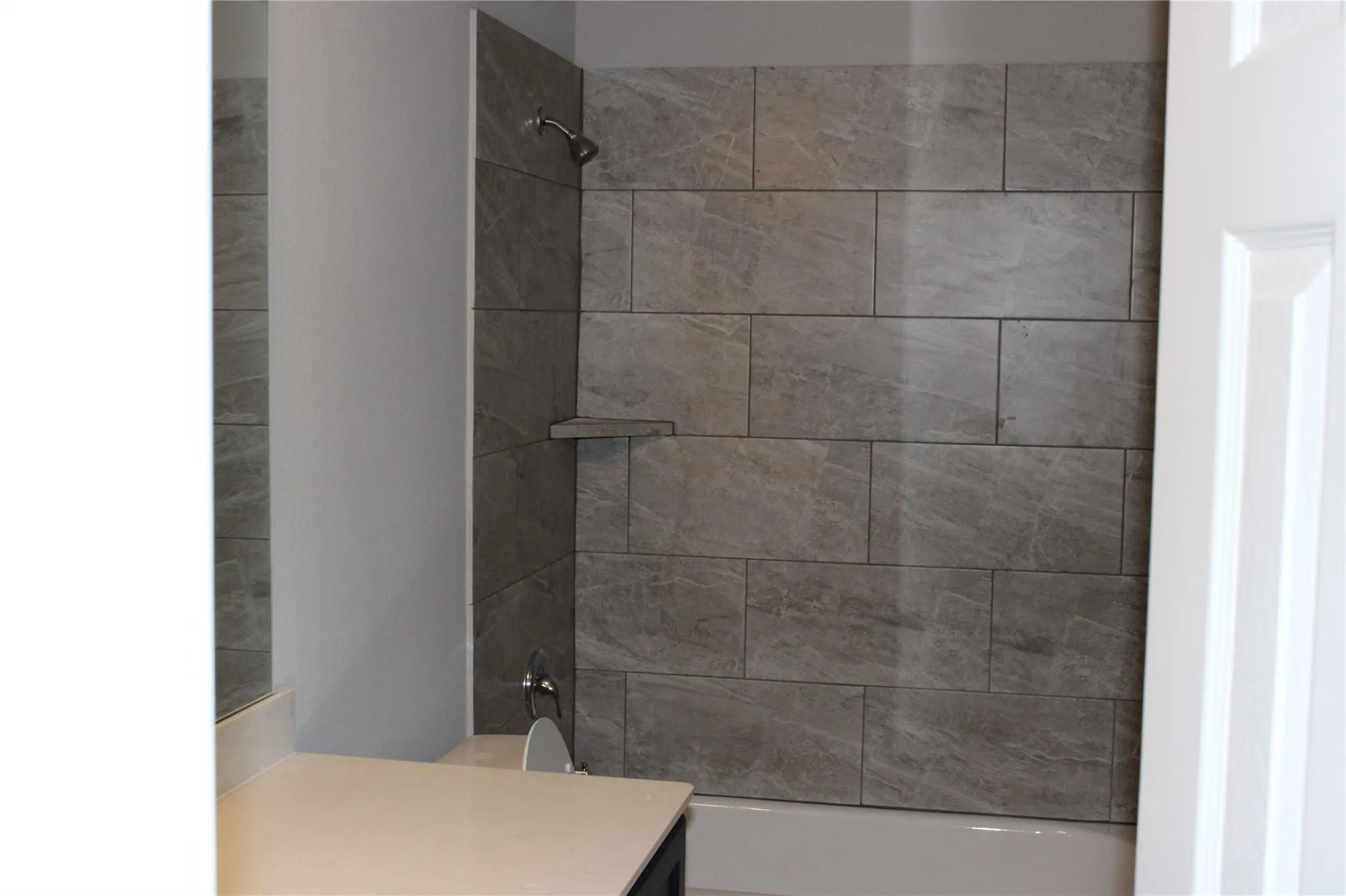 Tub and shower combination featuring large format tile surround, built-in shower shelf, and a shower head with handheld attachment