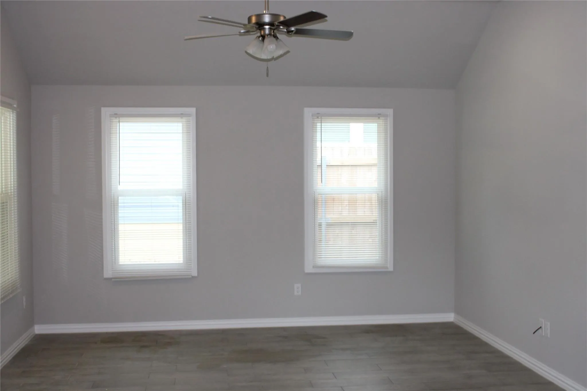 Vaulted ceiling with a brushed nickel ceiling fan, two double-hung windows, and wood-finish flooring