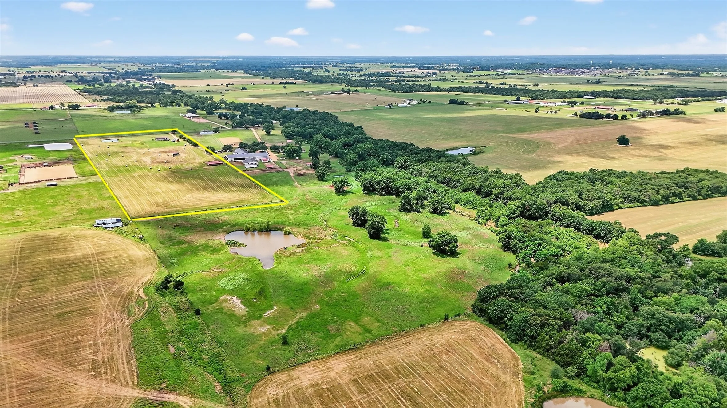 Expansive rural property featuring an established structure, cultivated fields, wooded areas, and a natural pond
