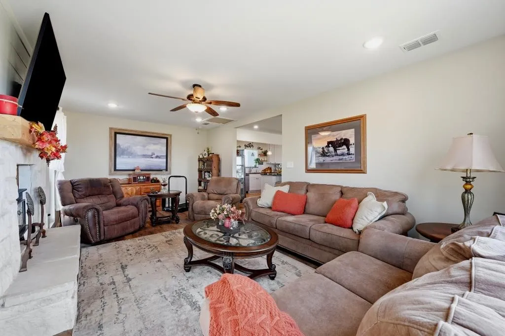 Spacious living room featuring multiple seating areas, ceiling fan with integrated lighting, wood-framed architectural details, and a round cocktail table with decorative base