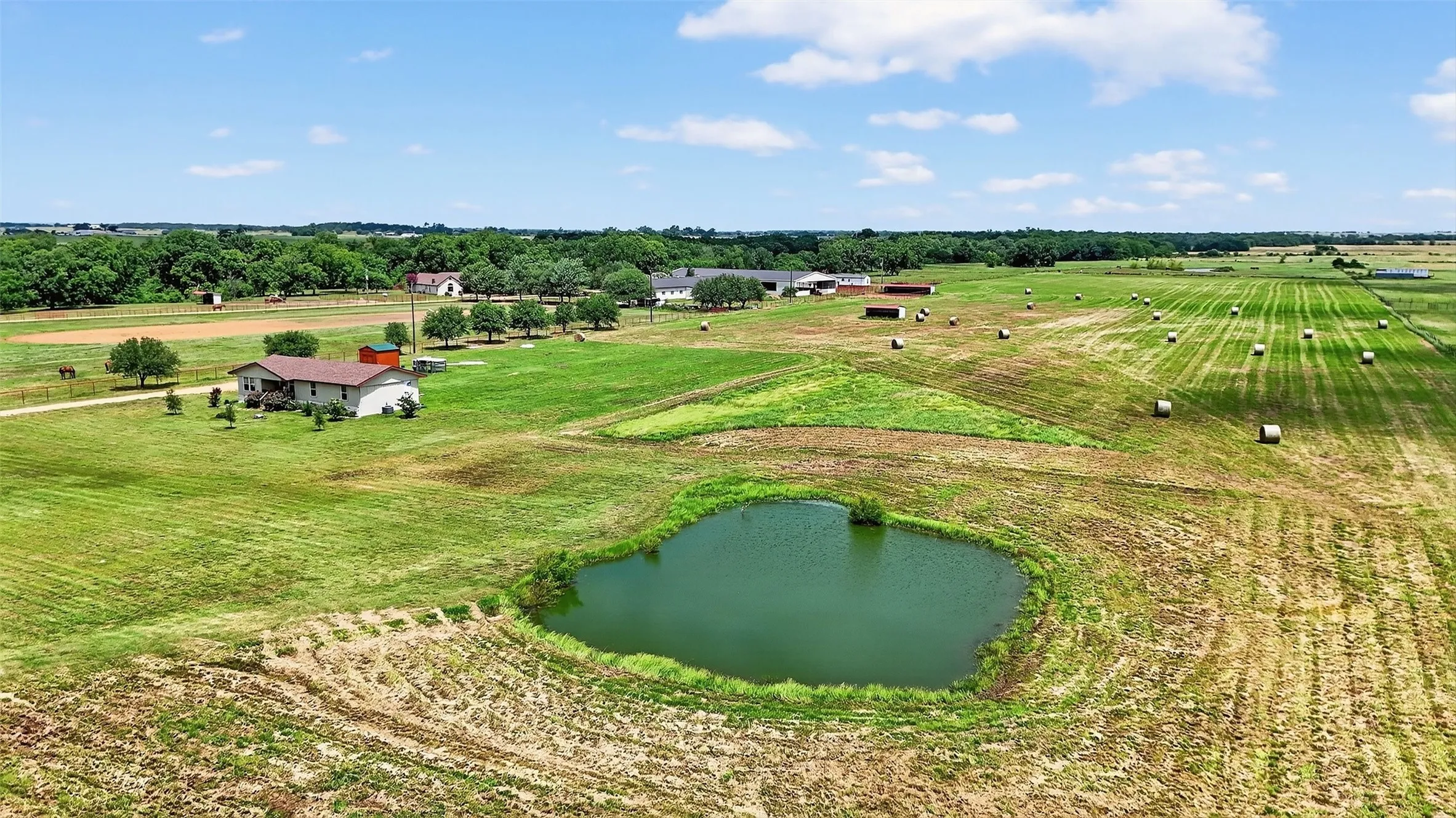 Expansive agricultural landscape featuring a pond, a residential structure, multiple outbuildings, and cultivated fields