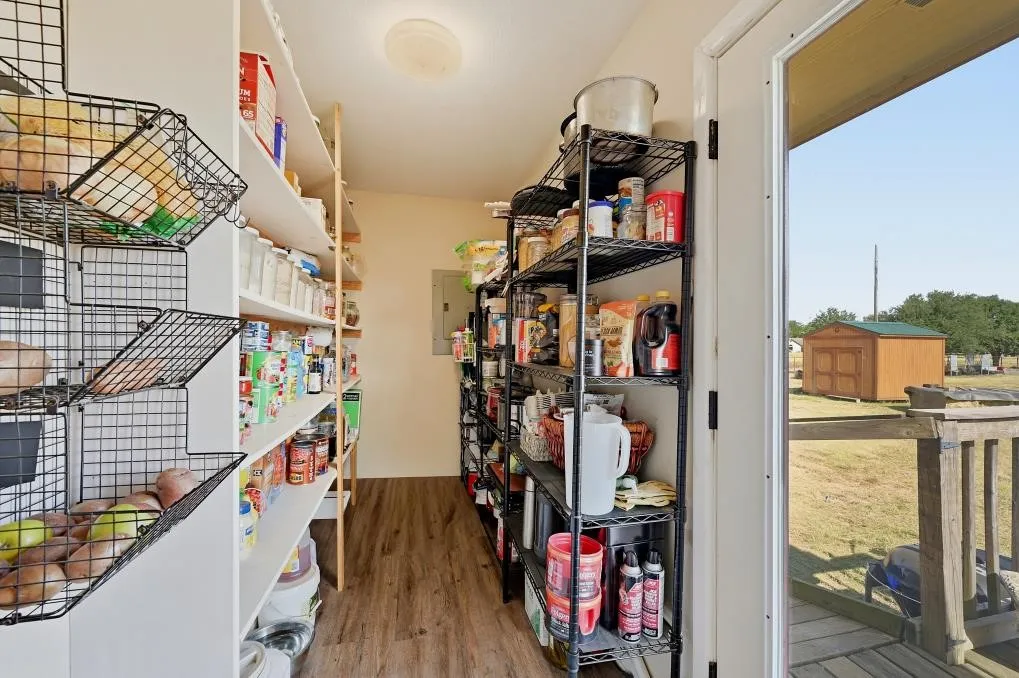 Walk-in pantry with extensive shelving, wood-finish flooring, and direct outdoor access