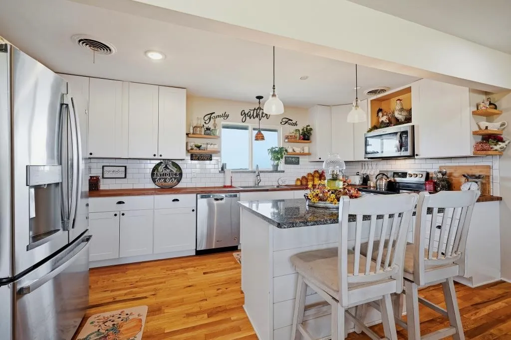 Stainless steel appliances, wood-finish flooring, white cabinetry, wood countertops, and a kitchen island with a granite surface