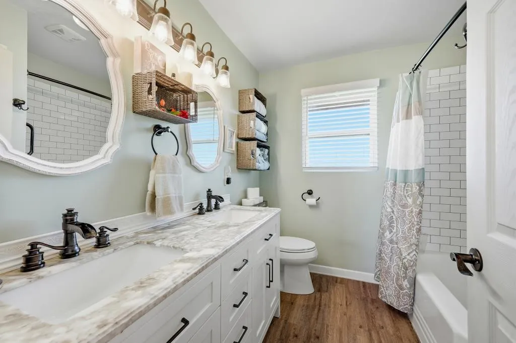 Dual vanity with white cabinetry, wood-finish flooring, a white subway tile bath surround, and a window with blinds
