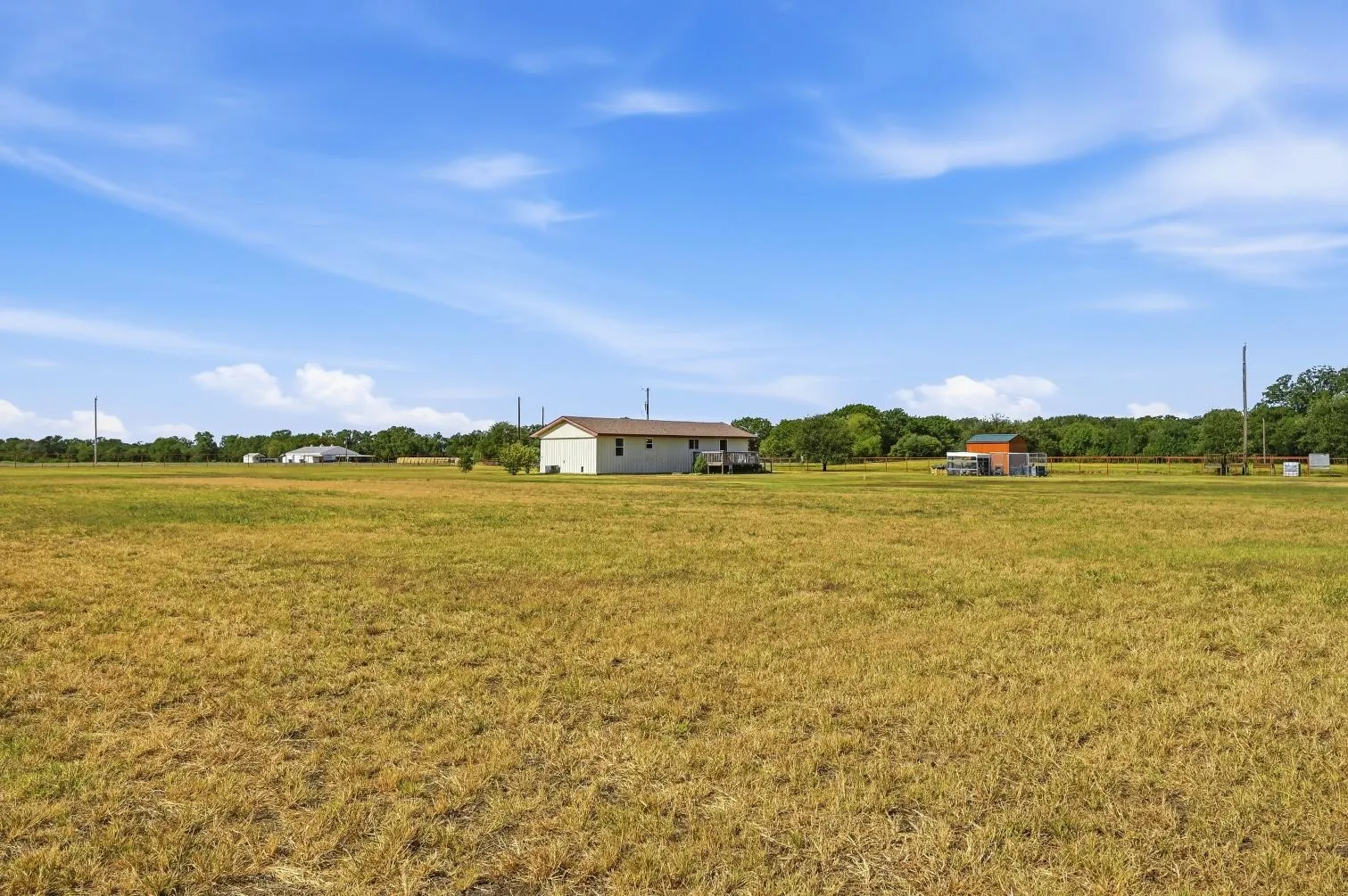 Expansive open field with a single-story residence featuring light-colored siding and a dark roof