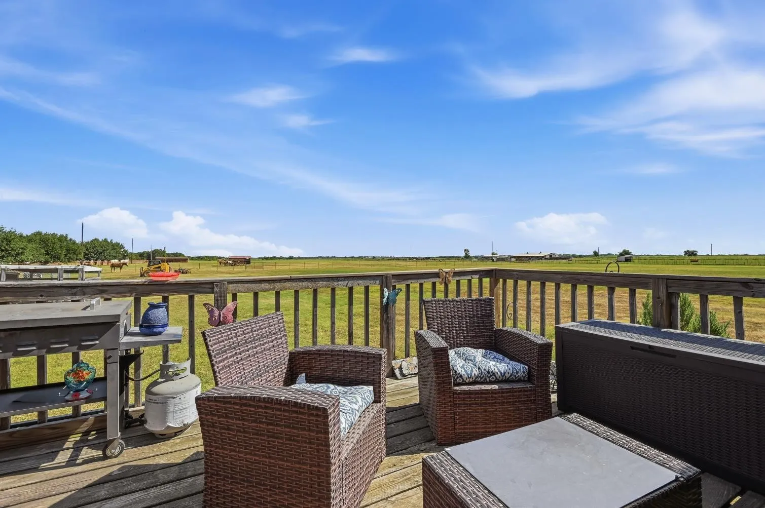 Expansive wood-finish deck with wood railings, overlooking open green fields
