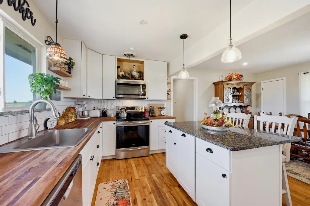 White cabinetry with black hardware, wood-finish countertops, stainless steel appliances, white subway tile backsplash, and a central island with a stone countertop