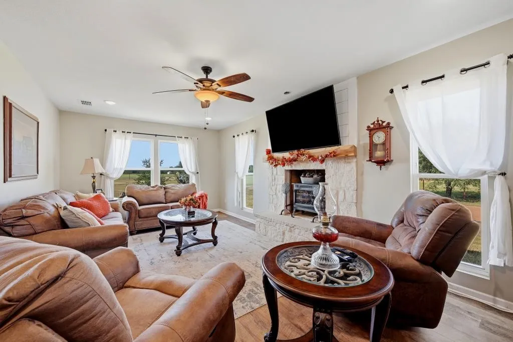 Living space featuring a stone fireplace with a wood mantle, ceiling fan, and wood-finish flooring