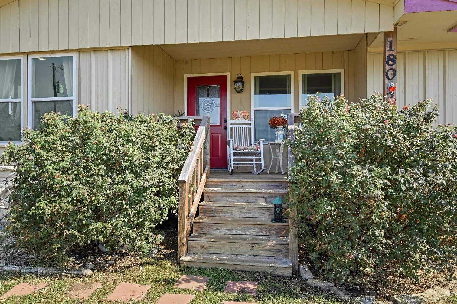 Entry porch with wood steps and railing, red front door, and light-colored siding