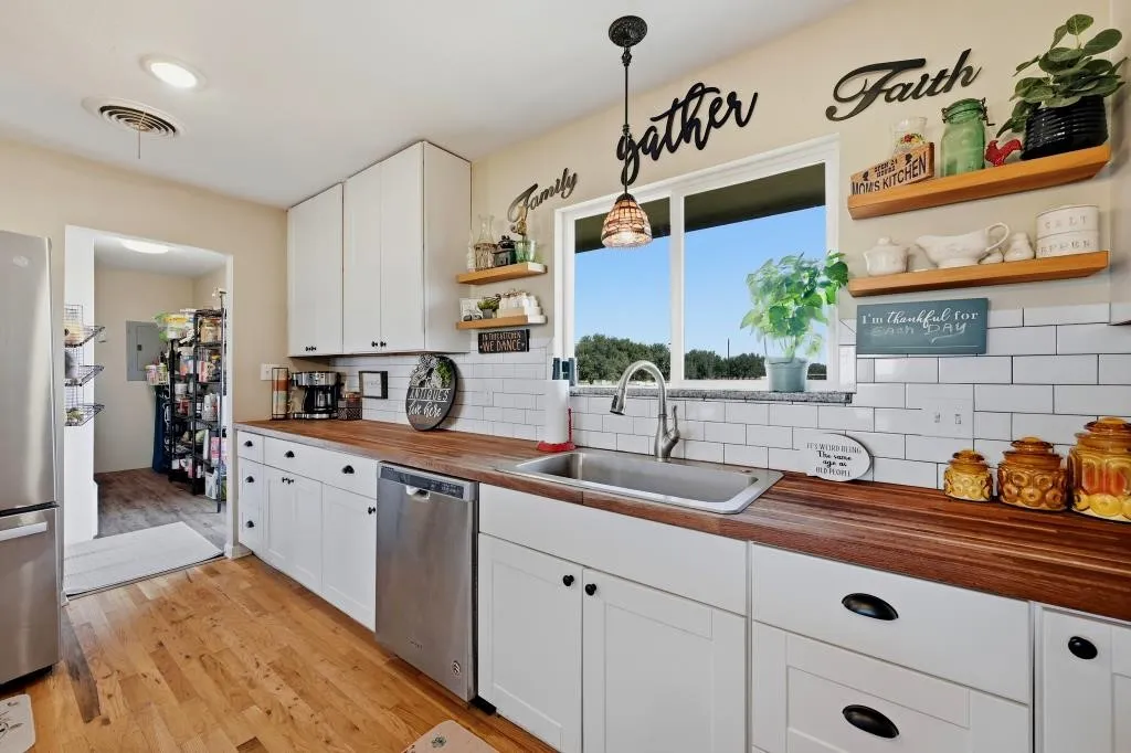 White shaker-style cabinetry, wood-finish countertops, subway tile backsplash, stainless steel appliances, and a window above the sink
