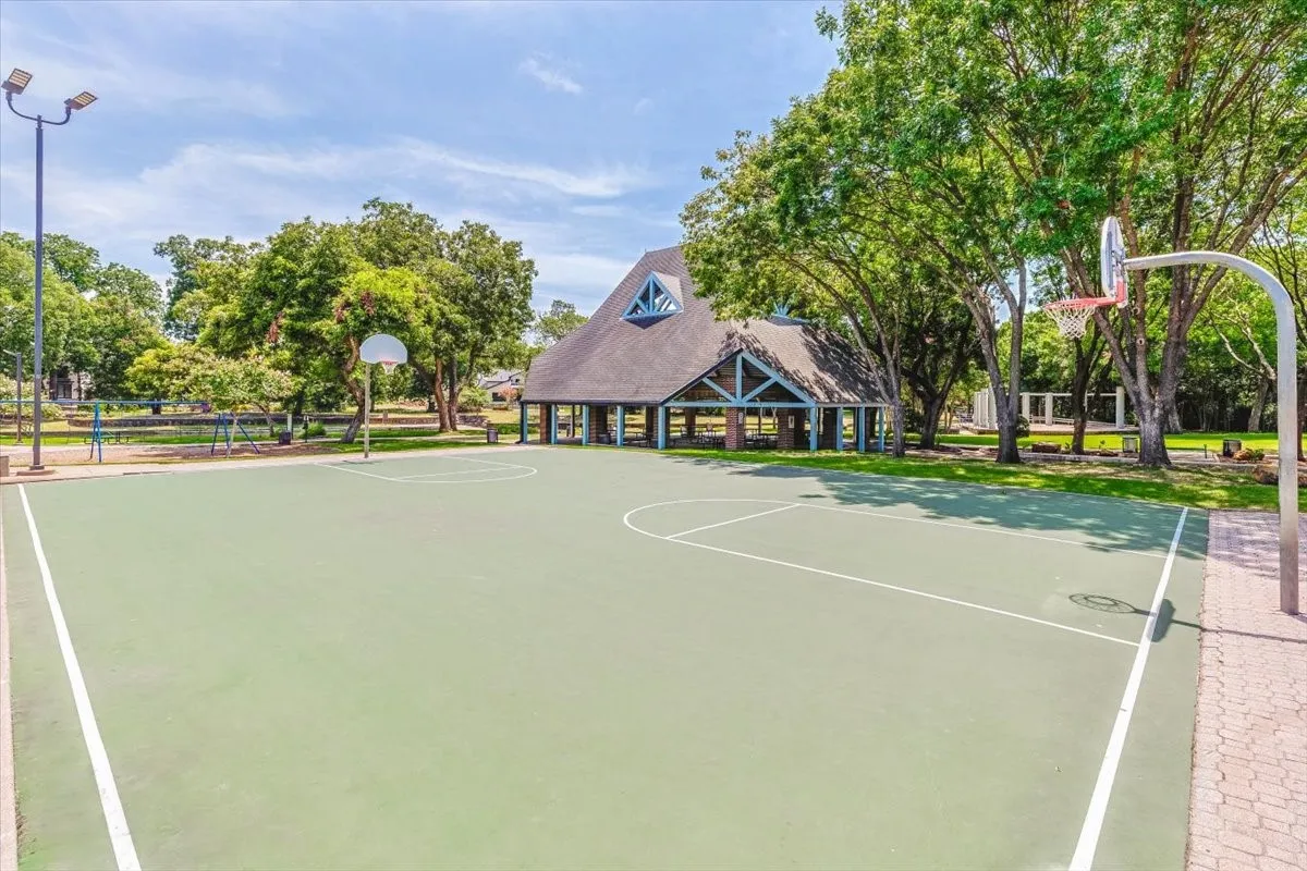 Outdoor athletic court with clear demarcation lines, two basketball hoops, and surrounding mature trees