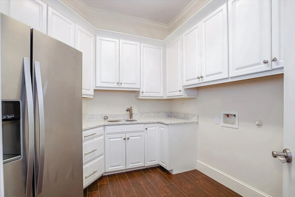 White cabinetry with brushed nickel hardware and stainless steel refrigerator, undermount sink, granite-style countertops.