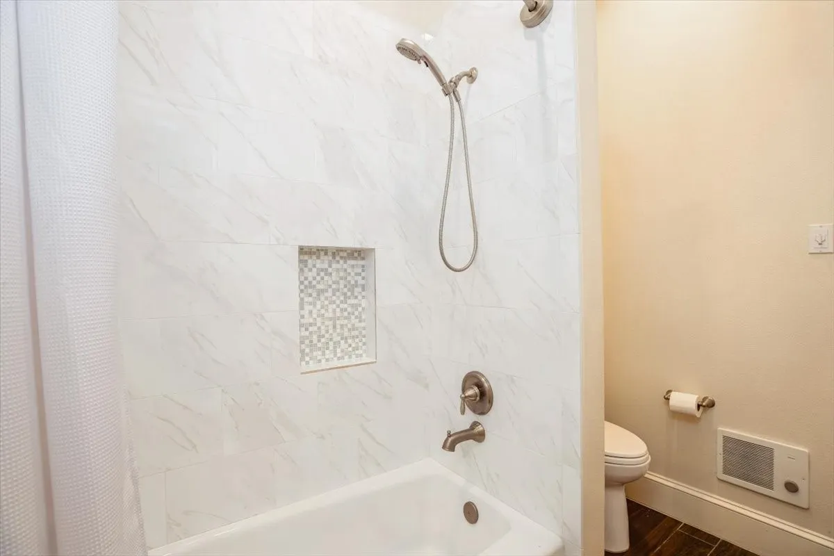 Jack and Jill Bathroom White marble tile shower surround with a mosaic tile niche, brushed nickel shower fixtures, and a white soaking tub