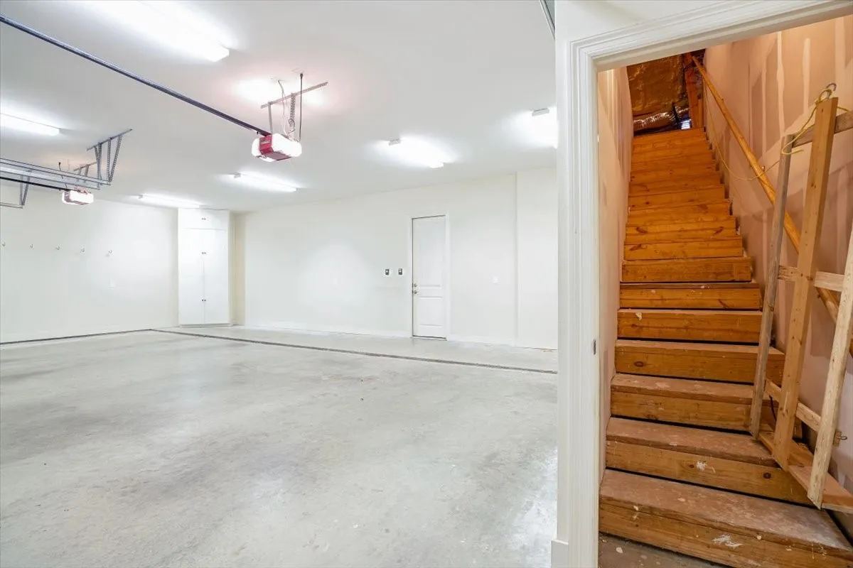 Spacious garage with concrete flooring, multiple overhead light fixtures, and built-in storage cabinetry