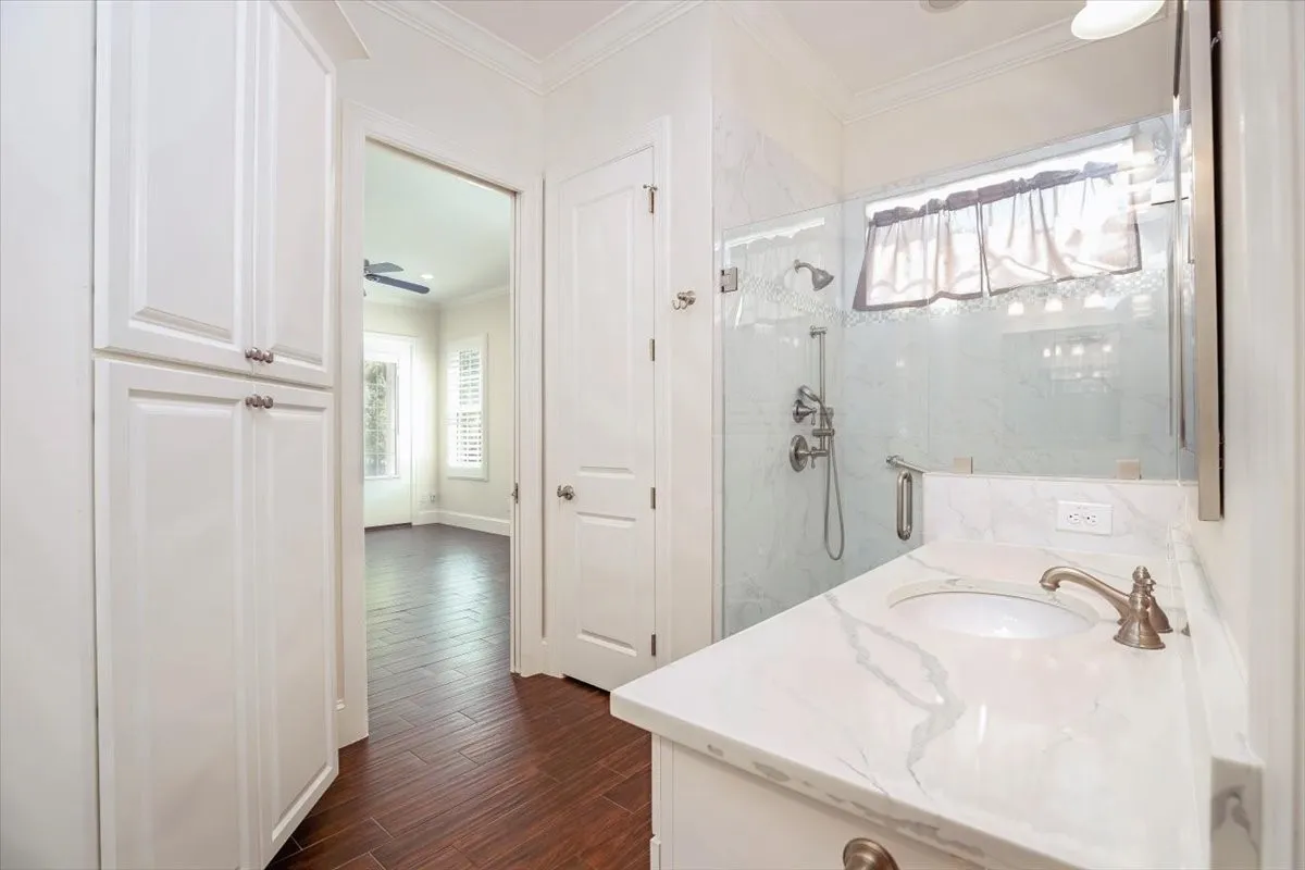 White shaker cabinetry, porcelain wood-finish flooring, glass-enclosed shower, white countertop, and single basin sink