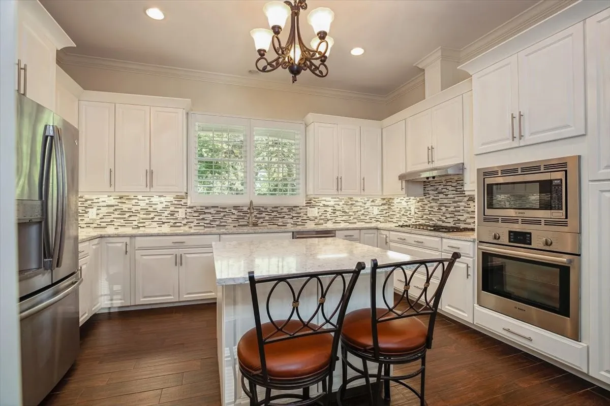 Kitchen featuring white cabinetry, stainless steel appliances, a tile backsplash, light-toned countertops, and porcelain wood-finish flooring