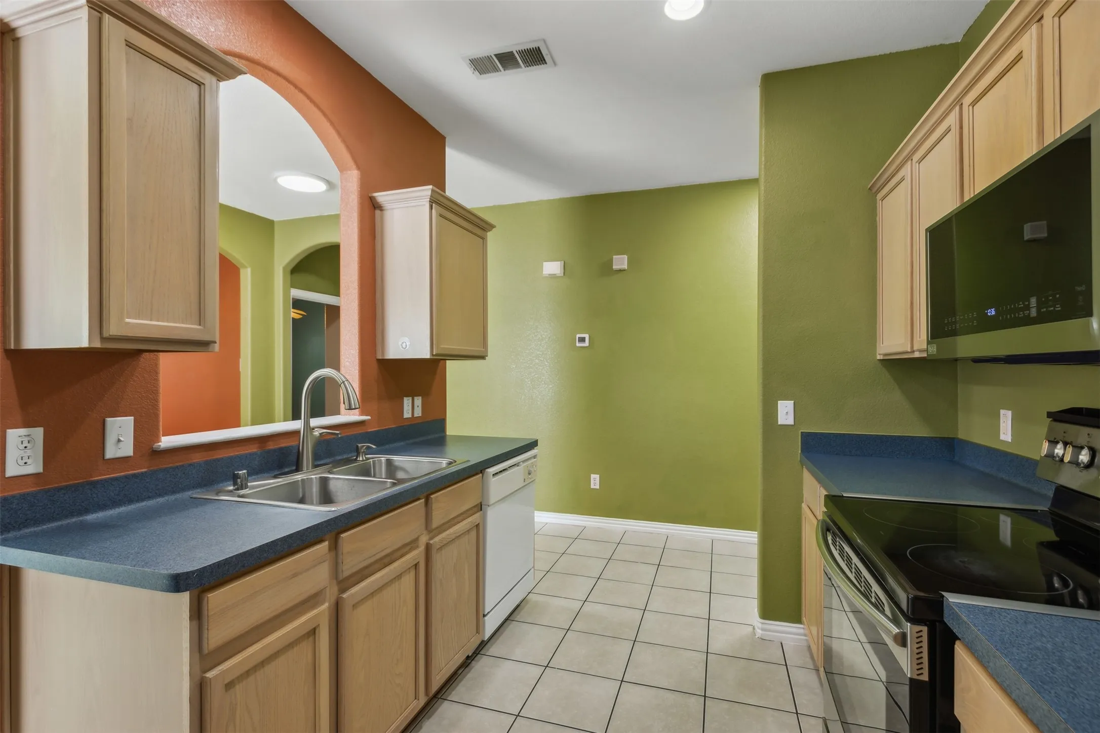 Kitchen with light brown cabinets, sink, light tile floors, and appliances with stainless steel finishes