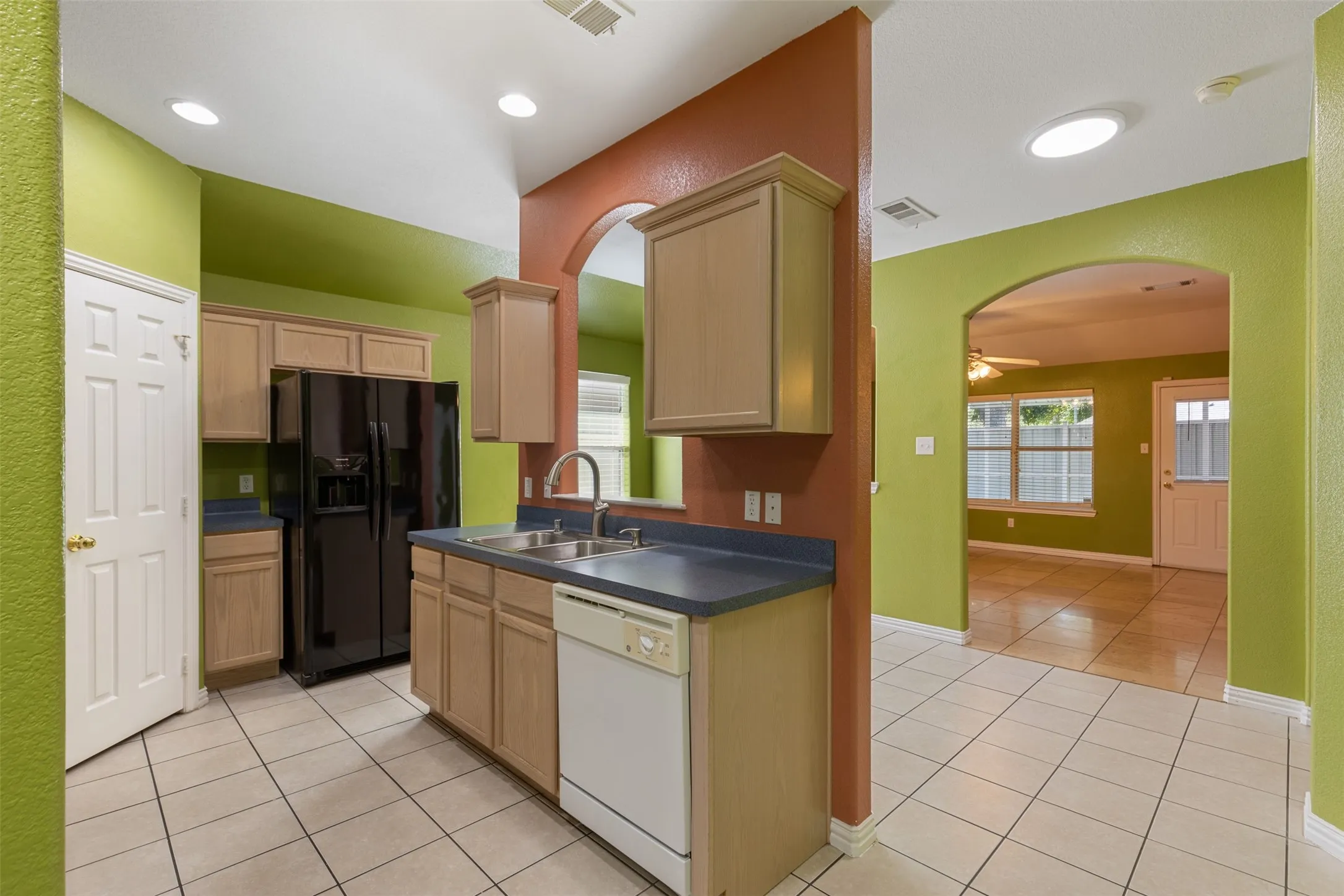 Kitchen with ceiling fan, black fridge, white dishwasher, light tile floors, and sink