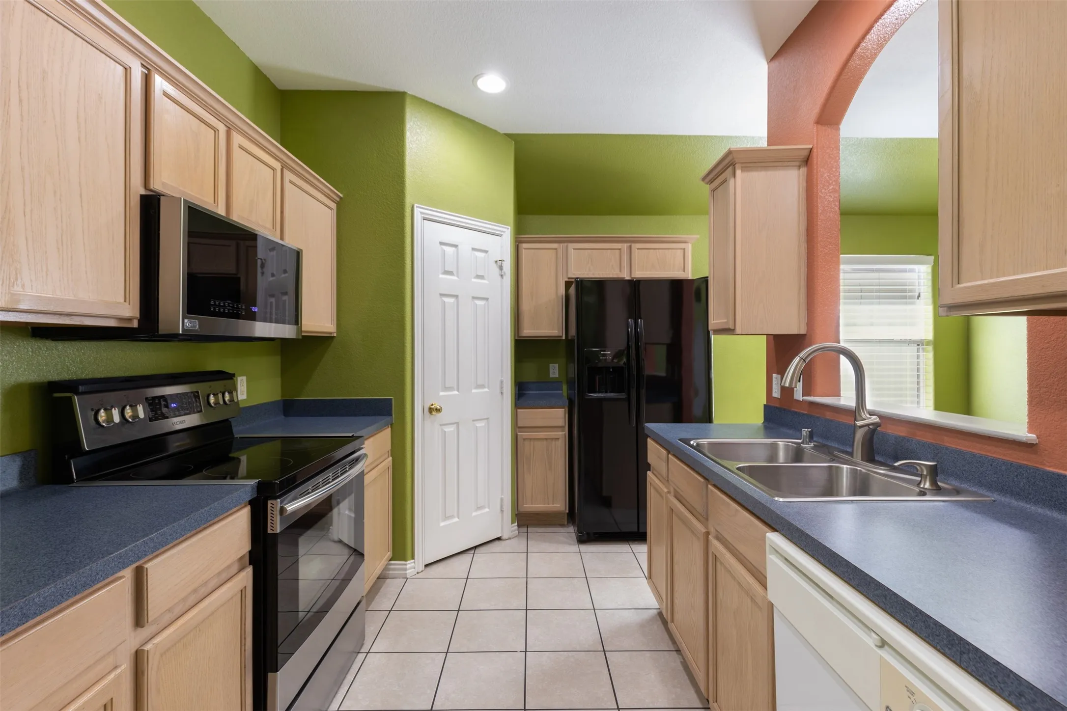 Kitchen featuring sink, light tile floors, light brown cabinetry, and appliances with stainless steel finishes
