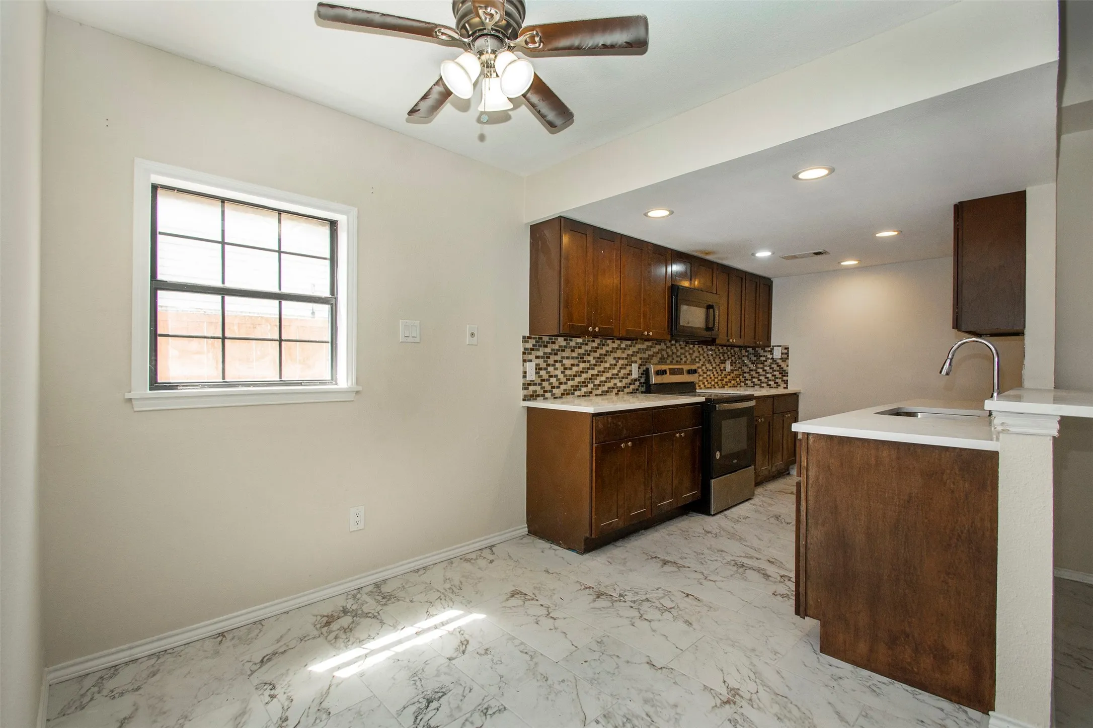 Kitchen featuring dark wood-finish cabinetry, white countertops, mosaic tile backsplash, and stainless steel appliances