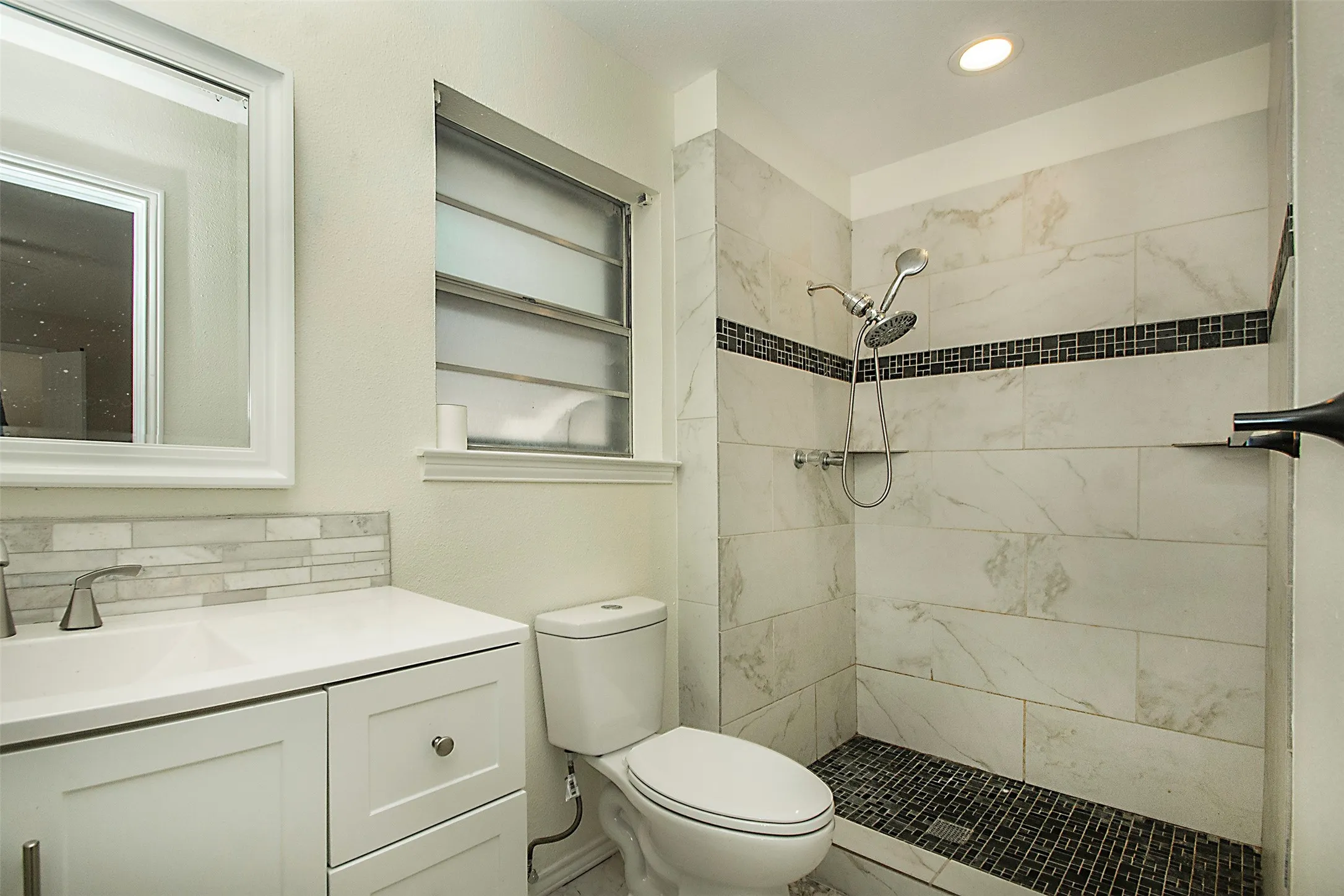 White vanity with integrated sink, sleek faucet, and tiled backsplash