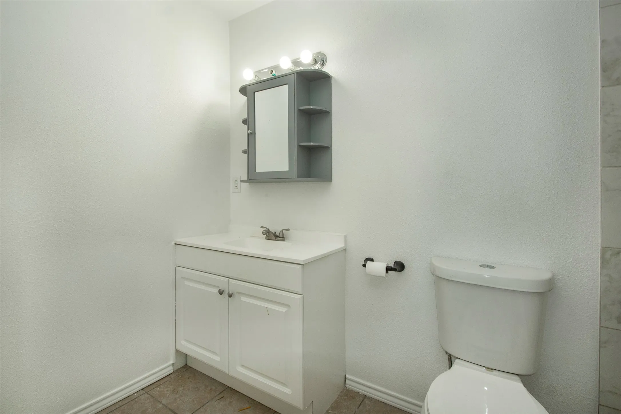 White vanity with integrated sink and cabinet storage, medicine cabinet with open shelving, and wall-mounted lighting fixture