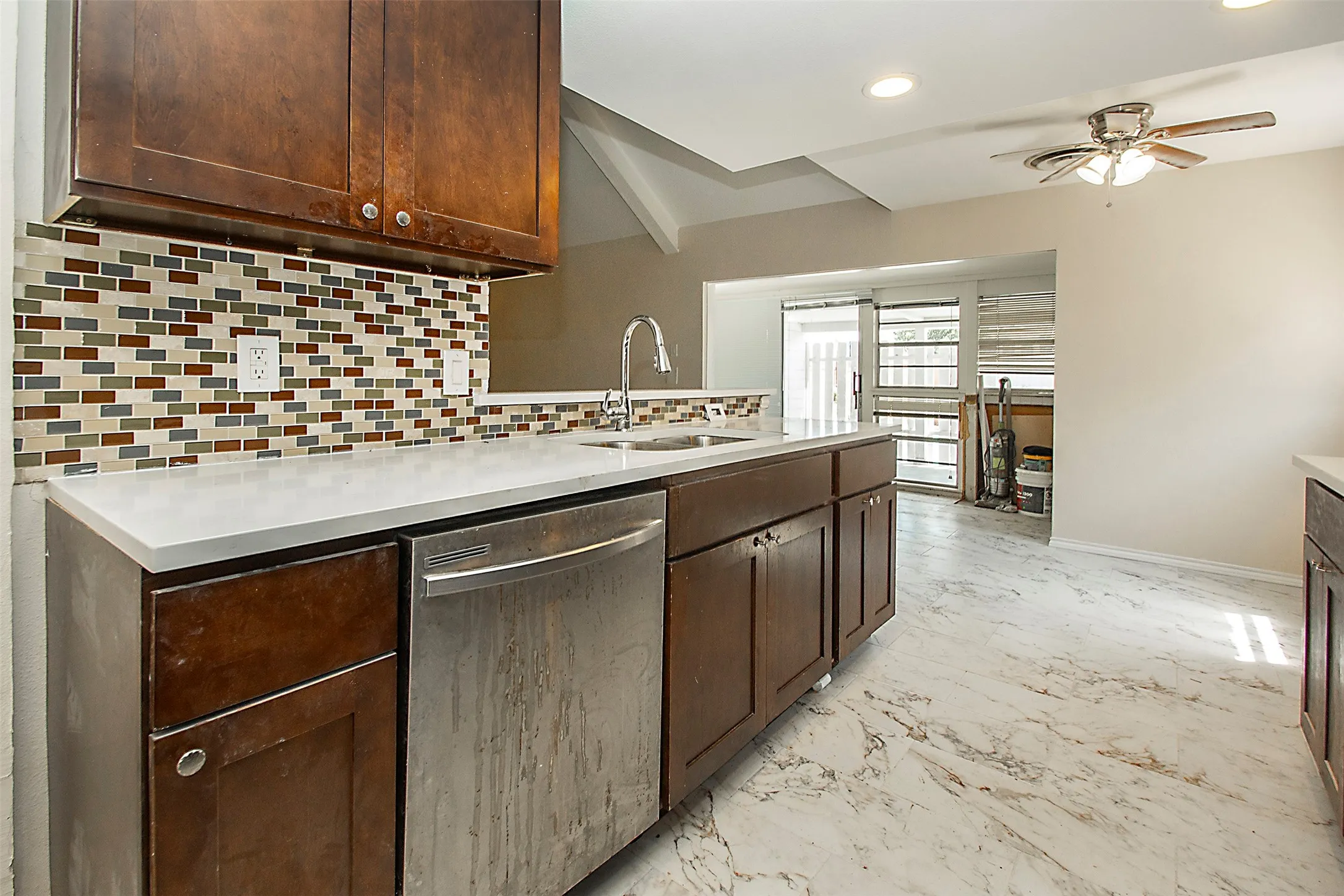 Kitchen featuring wood cabinetry, white countertops, mosaic tile backsplash, stainless steel dishwasher, and marble-look flooring
