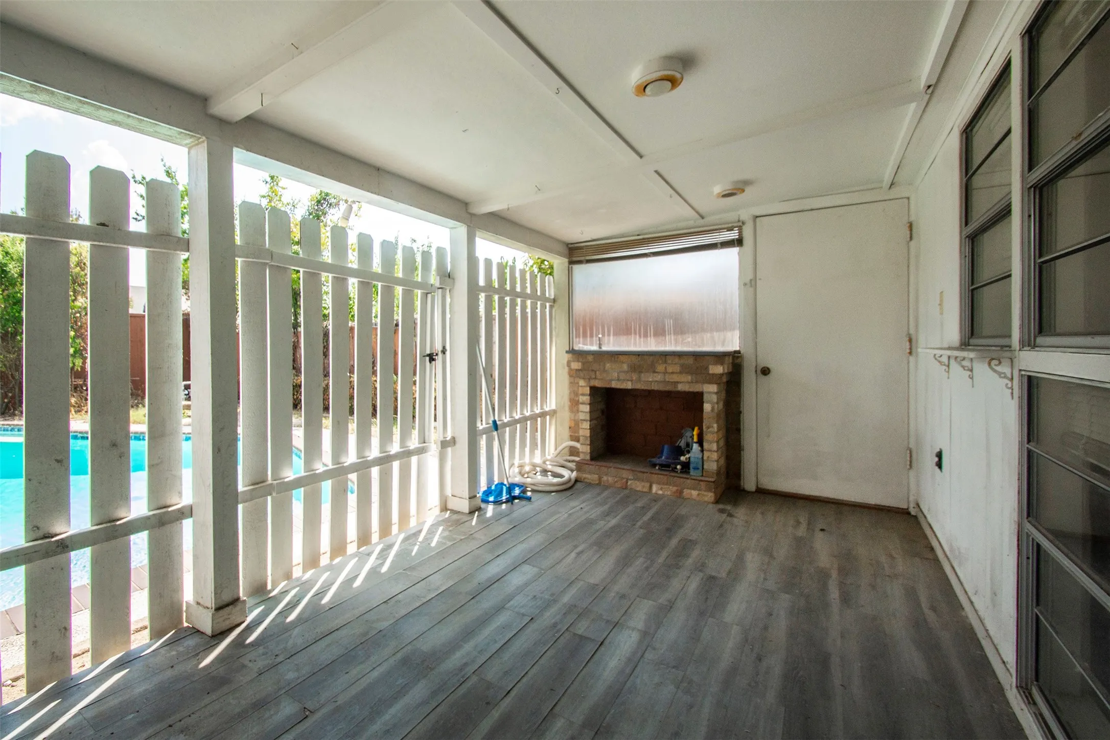 Covered outdoor area featuring wood-finish flooring, a brick fireplace, and direct access to a swimming pool