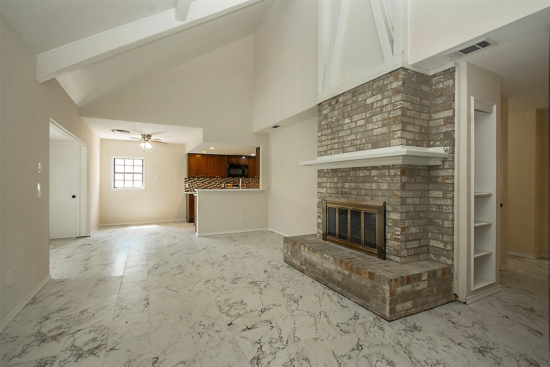 Vaulted ceiling with exposed beams, brick fireplace with mantel, built-in shelving, wood-finish cabinetry, and patterned floor tile