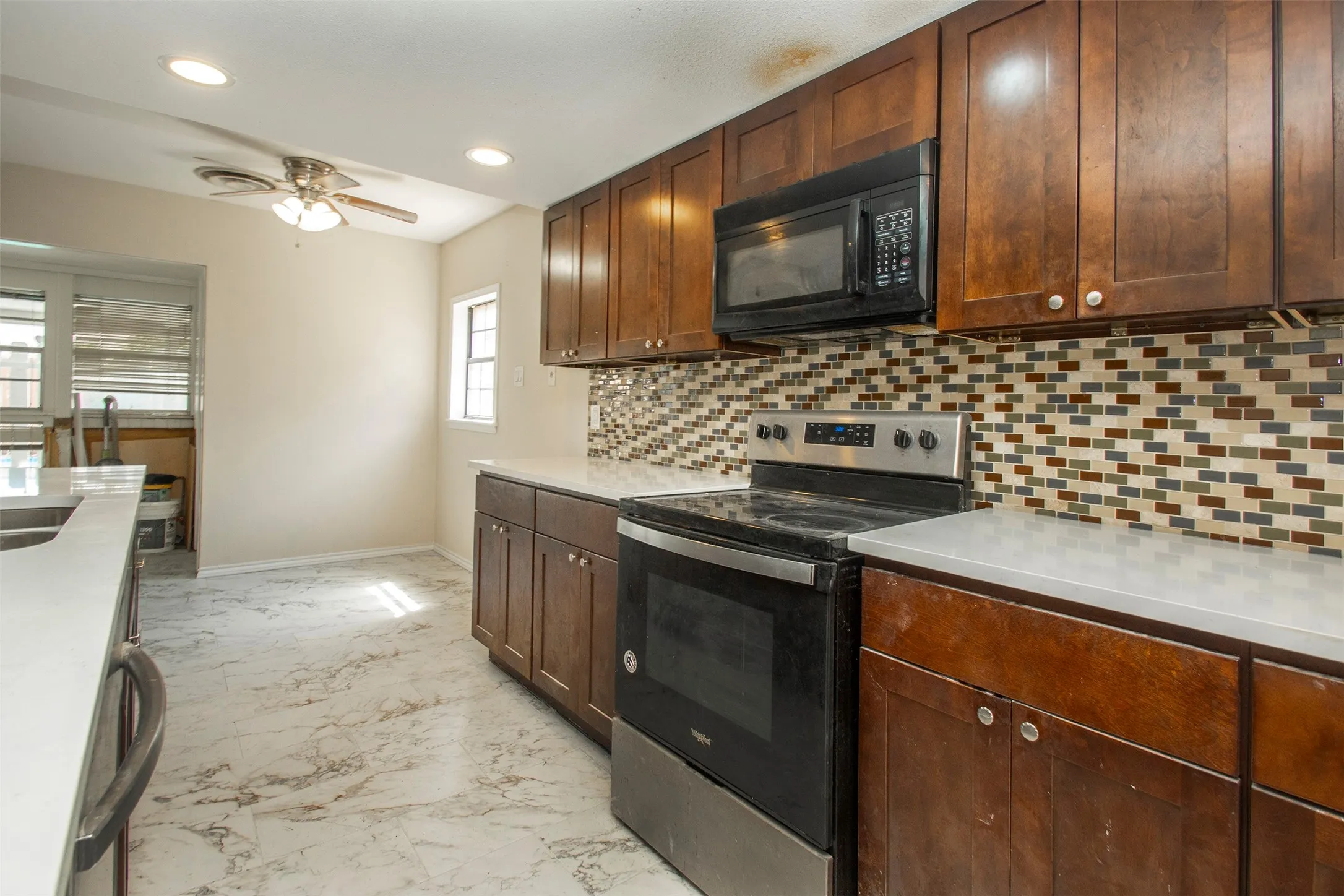 Dark wood-finish cabinetry, patterned tile backsplash, stainless steel and black range, built-in microwave, and light-toned countertops