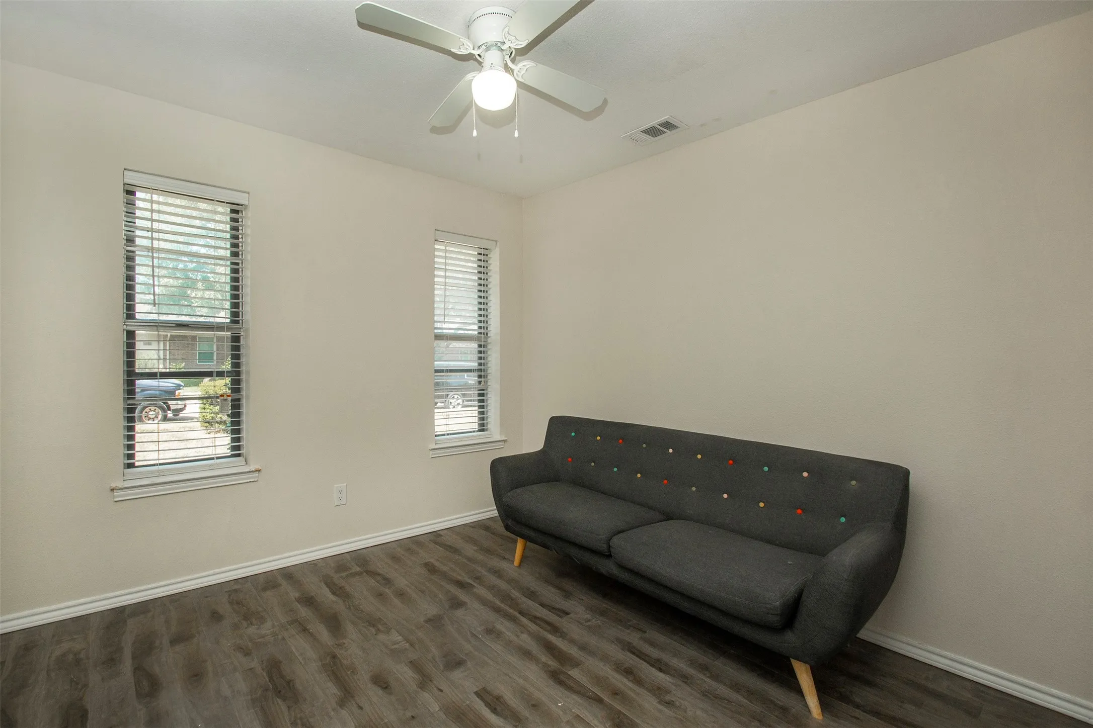 Interior room featuring wood-finish flooring, light-toned walls, two windows with blinds, and a ceiling fan with integrated lighting