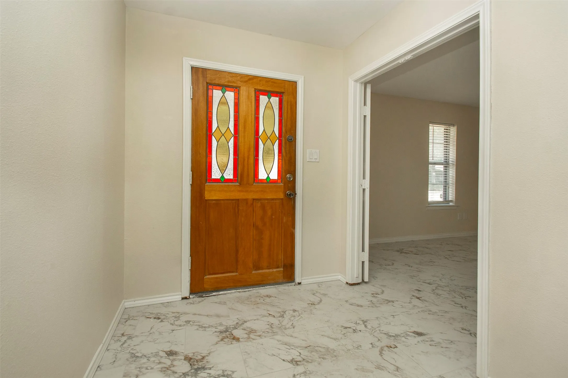 Entryway featuring a wood-panel door with decorative glass inserts, light-toned walls, and marble-look flooring