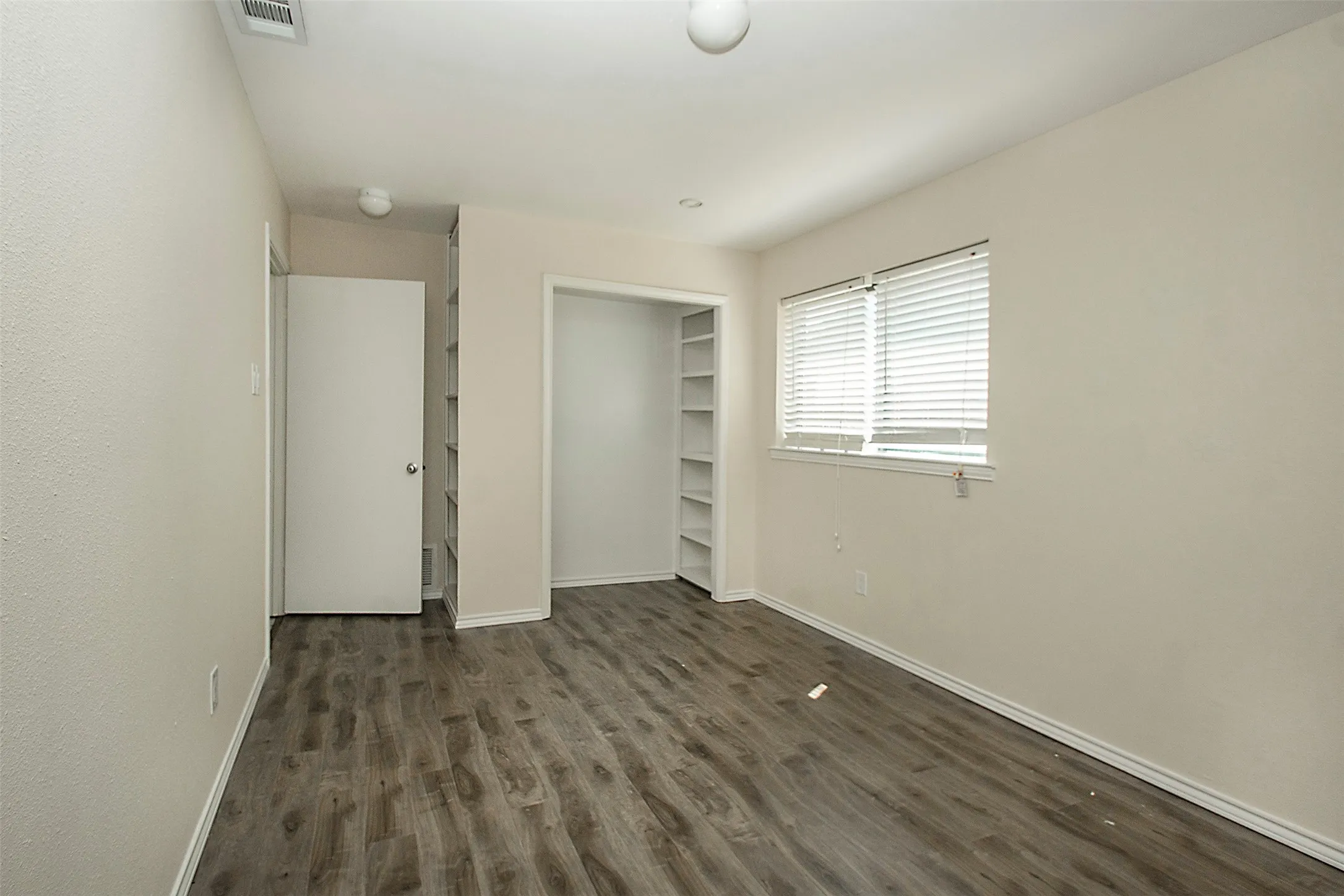 Wood-finish flooring, built-in shelving, window with blinds, and flush-mounted ceiling lighting