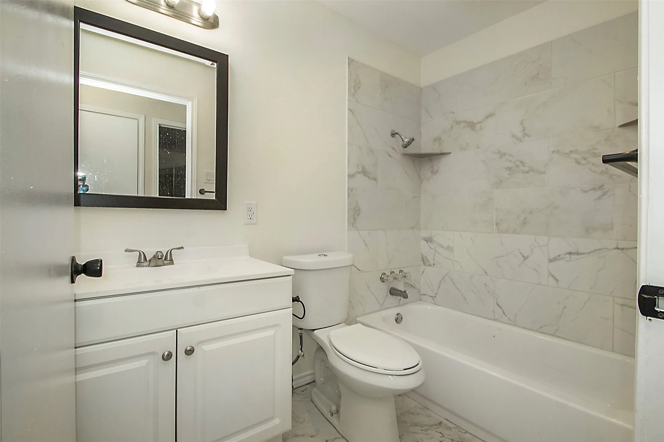 White vanity with an integrated sink and brushed nickel faucet, large framed mirror, tiled flooring, and a tub/shower combination with a tiled surround