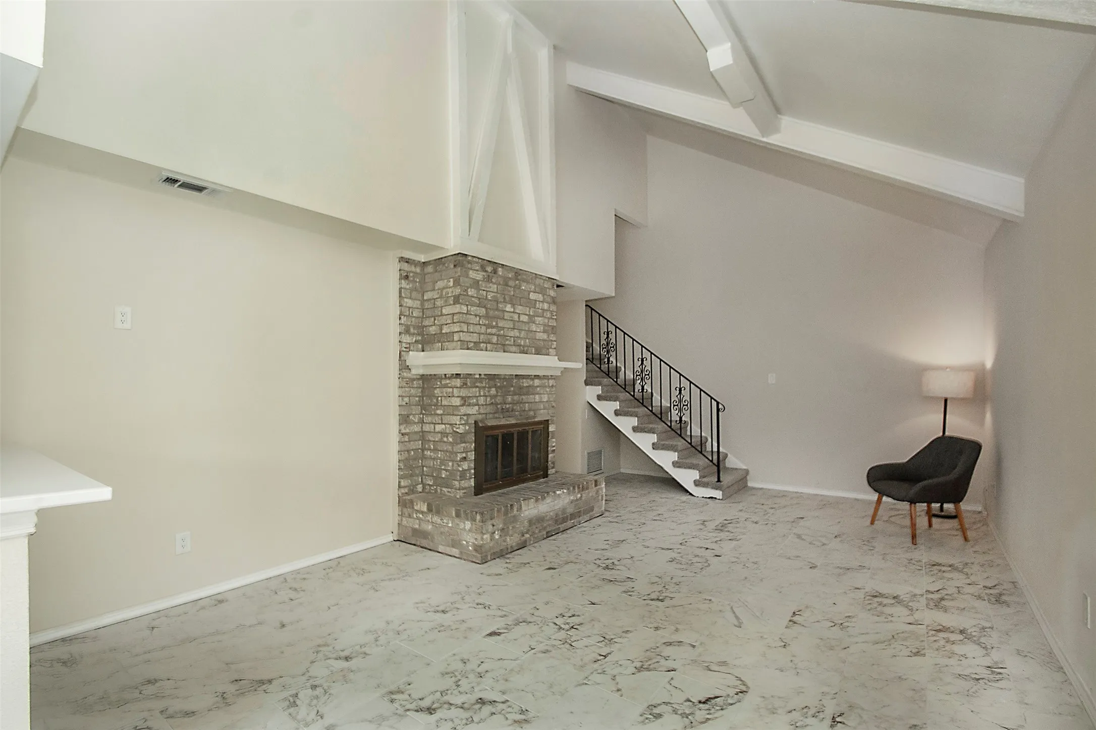 Vaulted ceiling with exposed beams, brick fireplace with mantel, and a staircase featuring an ornate metal railing