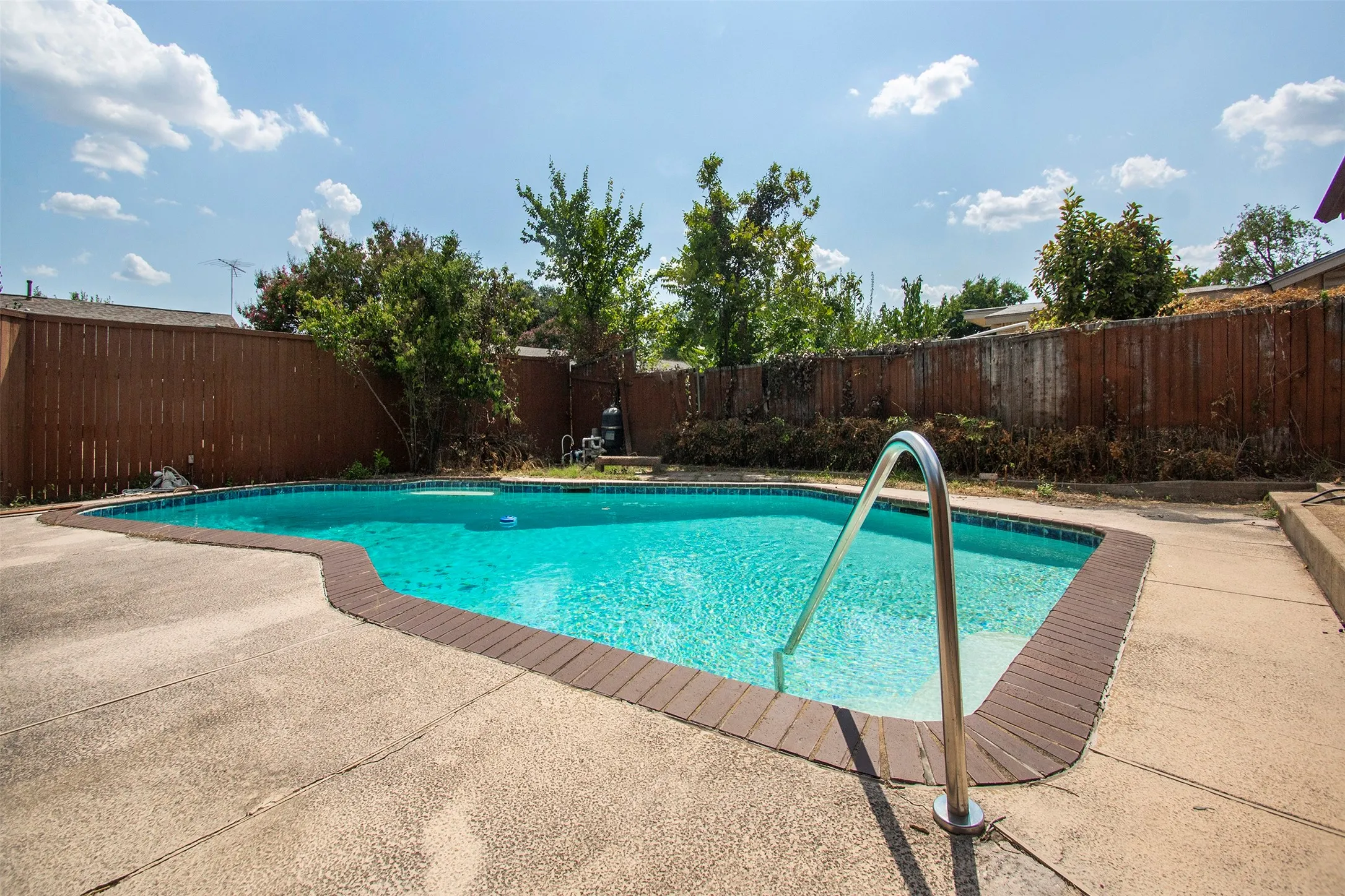 In-ground swimming pool with a curved concrete deck and perimeter brick coping